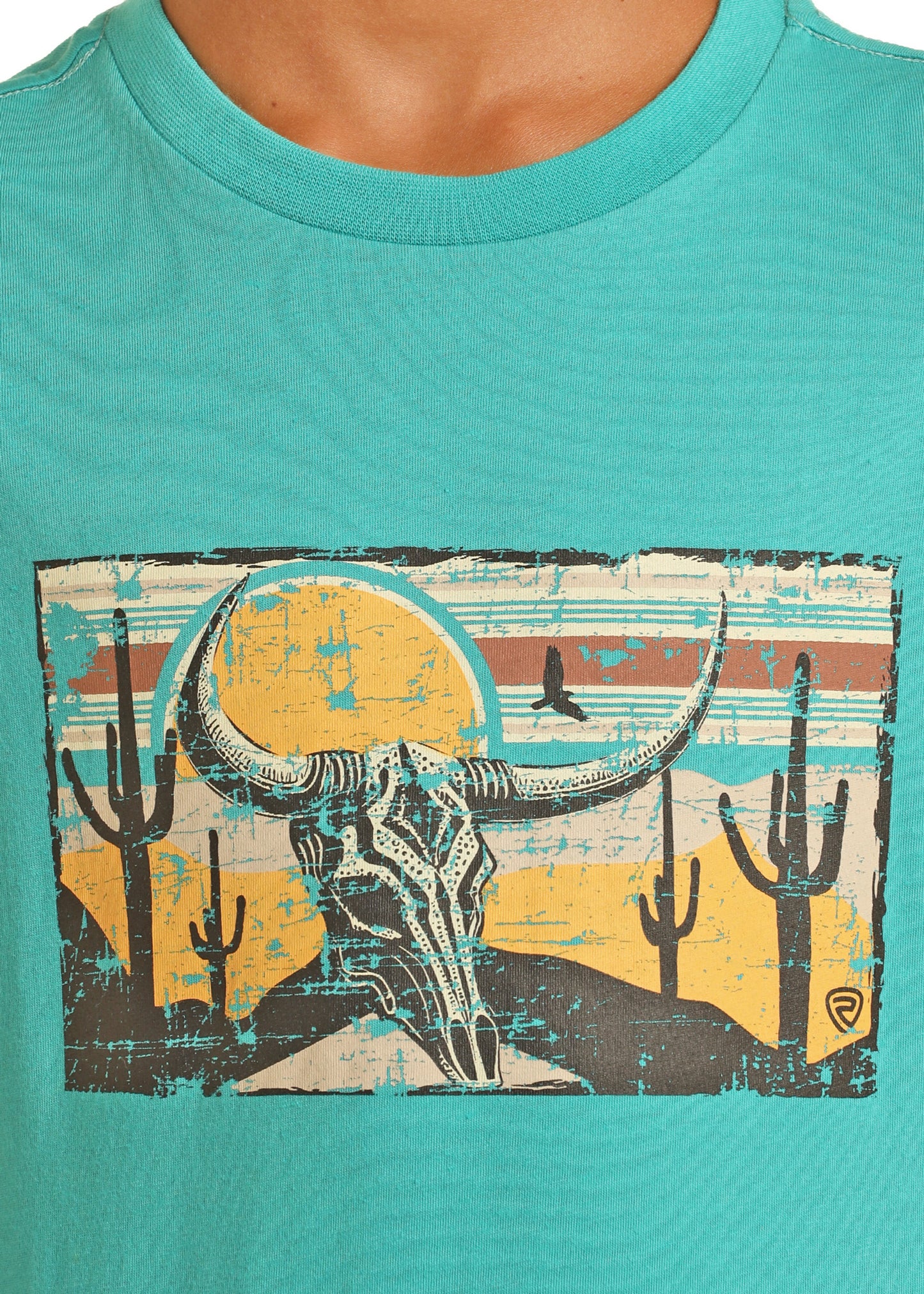 The Rock & Roll Denim Boys' Skull Graphic T-Shirt features a southwestern steer skull with large horns, desert cacti, hills, and a setting sun on a vibrant turquoise tee.