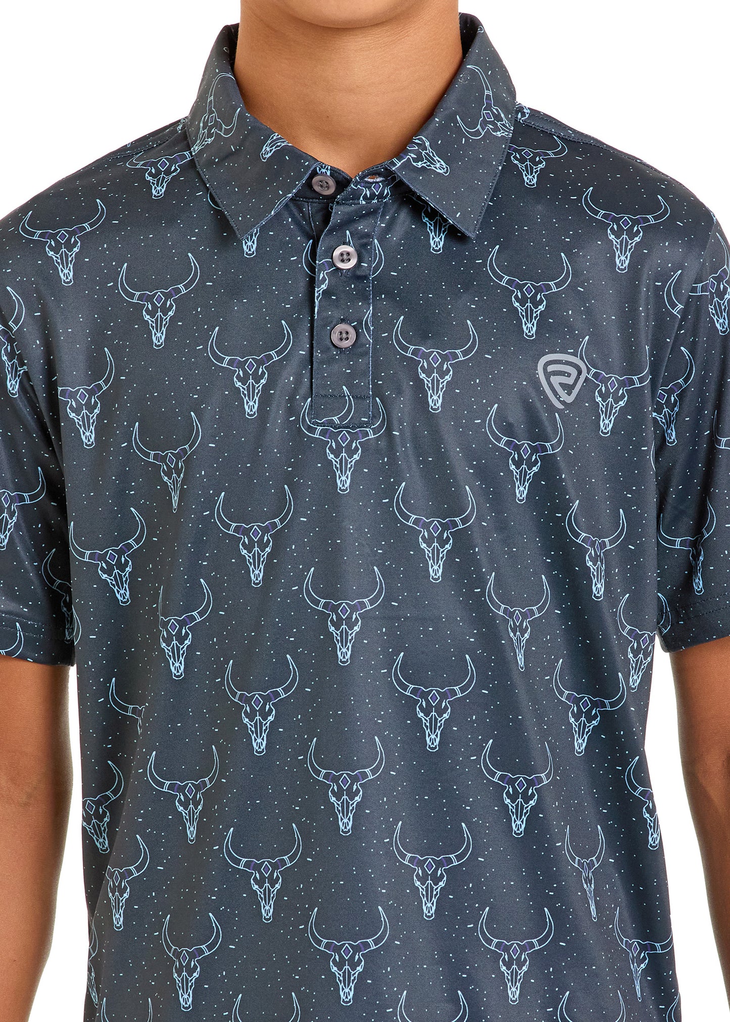 A person is shown from the waist up wearing a Boys' Longhorn Skulls Polo by Rock & Roll Denim, featuring a dark blue color and a repeating pattern of bull skulls with small dots.