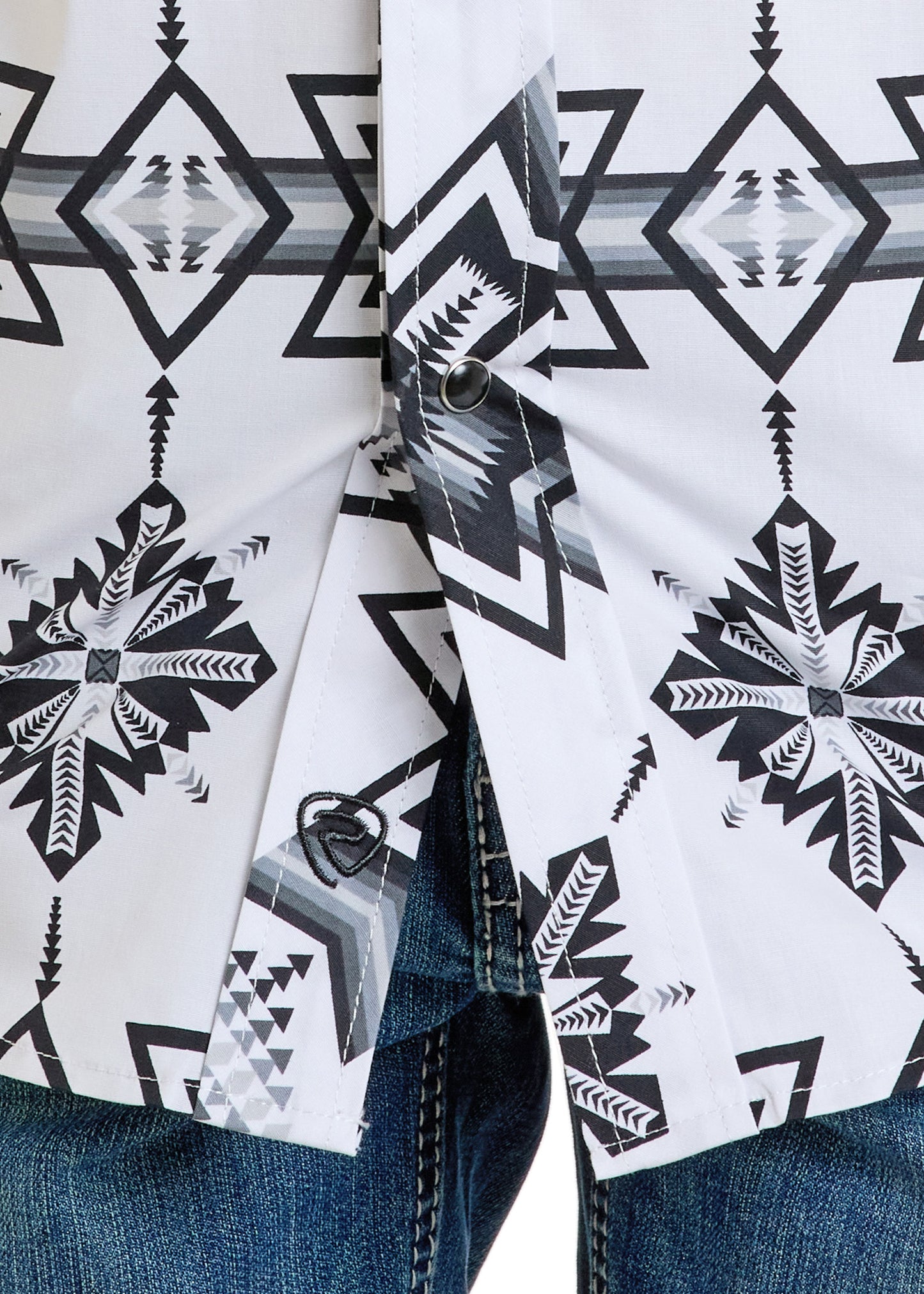 A close-up of a person wearing the Rock & Roll Denim Boys' Black & White Aztec Long Sleeve Snap Shirt with black geometric patterns, paired with blue denim jeans. The shirt is fastened at the bottom.