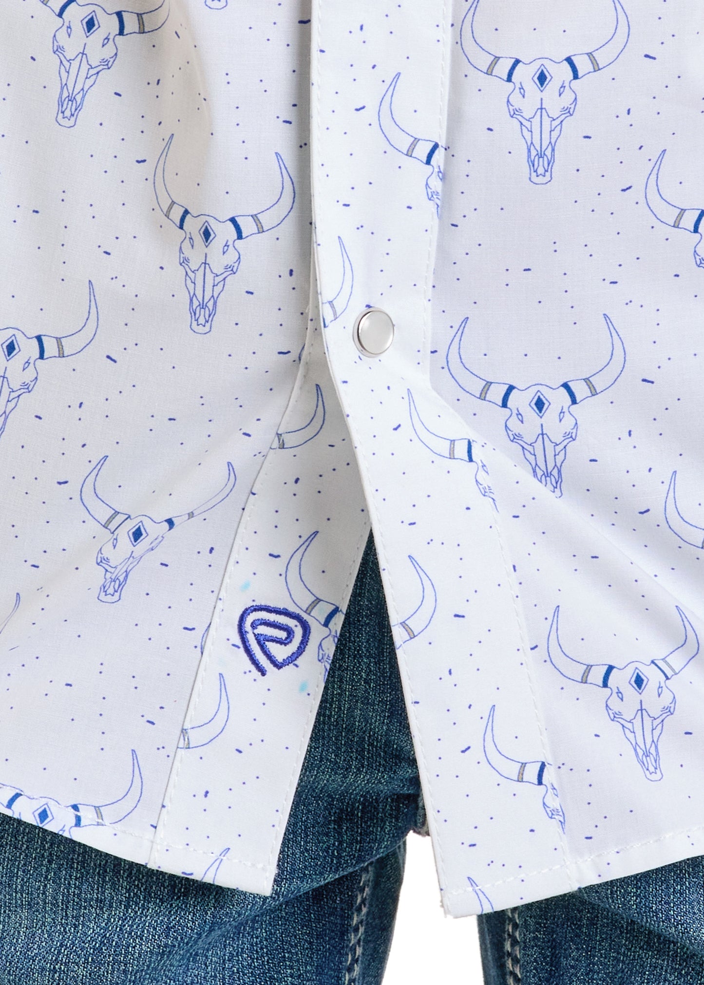 Close-up of the Rock & Roll Denim Boys' White Longhorn Long Sleeve Snap Shirt, showcasing a blue bull skull pattern, blue speckles, and a metal snap button, paired with blue jeans at the bottom.