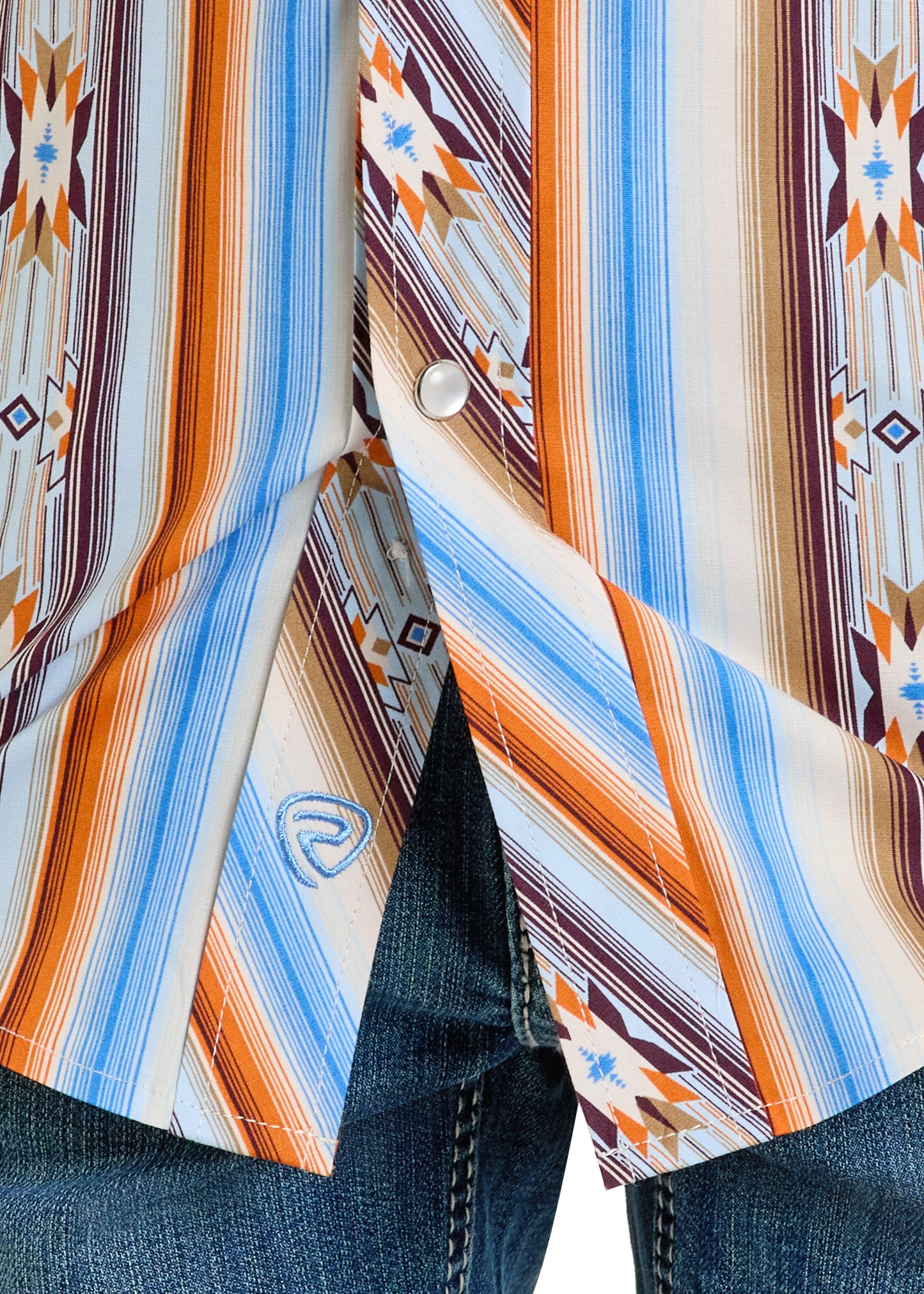 A close-up of the Rock & Roll Denim Boys' Multi Striped Aztec Long Sleeve Snap Shirt, featuring orange, blue, brown, and white geometric stripes, worn over blue jeans.