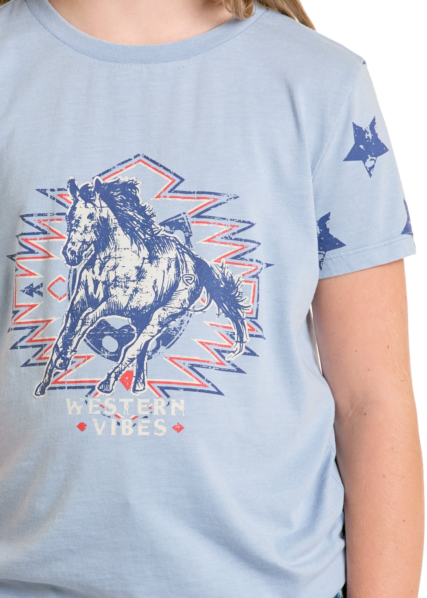 A girl wears the Rock & Roll Denim Girls' Western Vibes Graphic Tee, featuring a galloping horse, geometric patterns, and "WESTERN VIBES" on the front, plus a blue star accent on the sleeve.