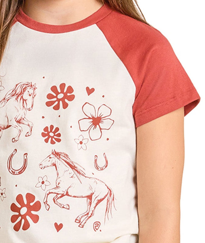 A child wears the Rock & Roll Denim Girls' Raglan Sleeve Horse Graphic Tee featuring red sleeves and a cream front with red horse illustrations, flowers, horseshoes, and hearts.
