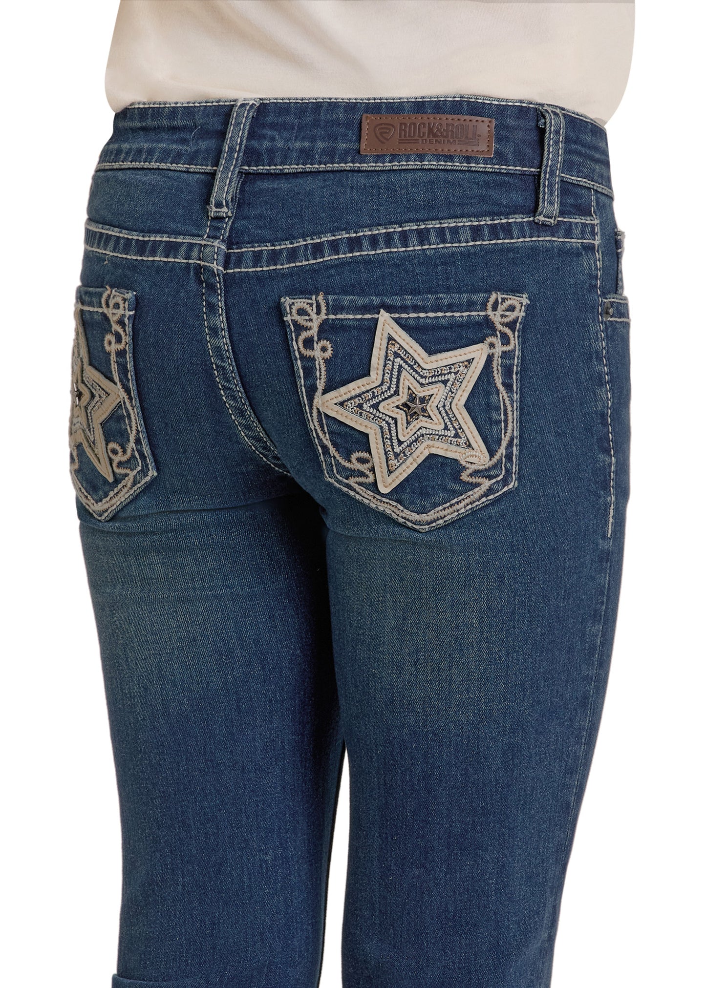 A person wearing Rock & Roll Denim Girls' Star Bootcut Jeans in blue, featuring white star embroidery on the back pockets and a brown leather brand patch on the waistband.