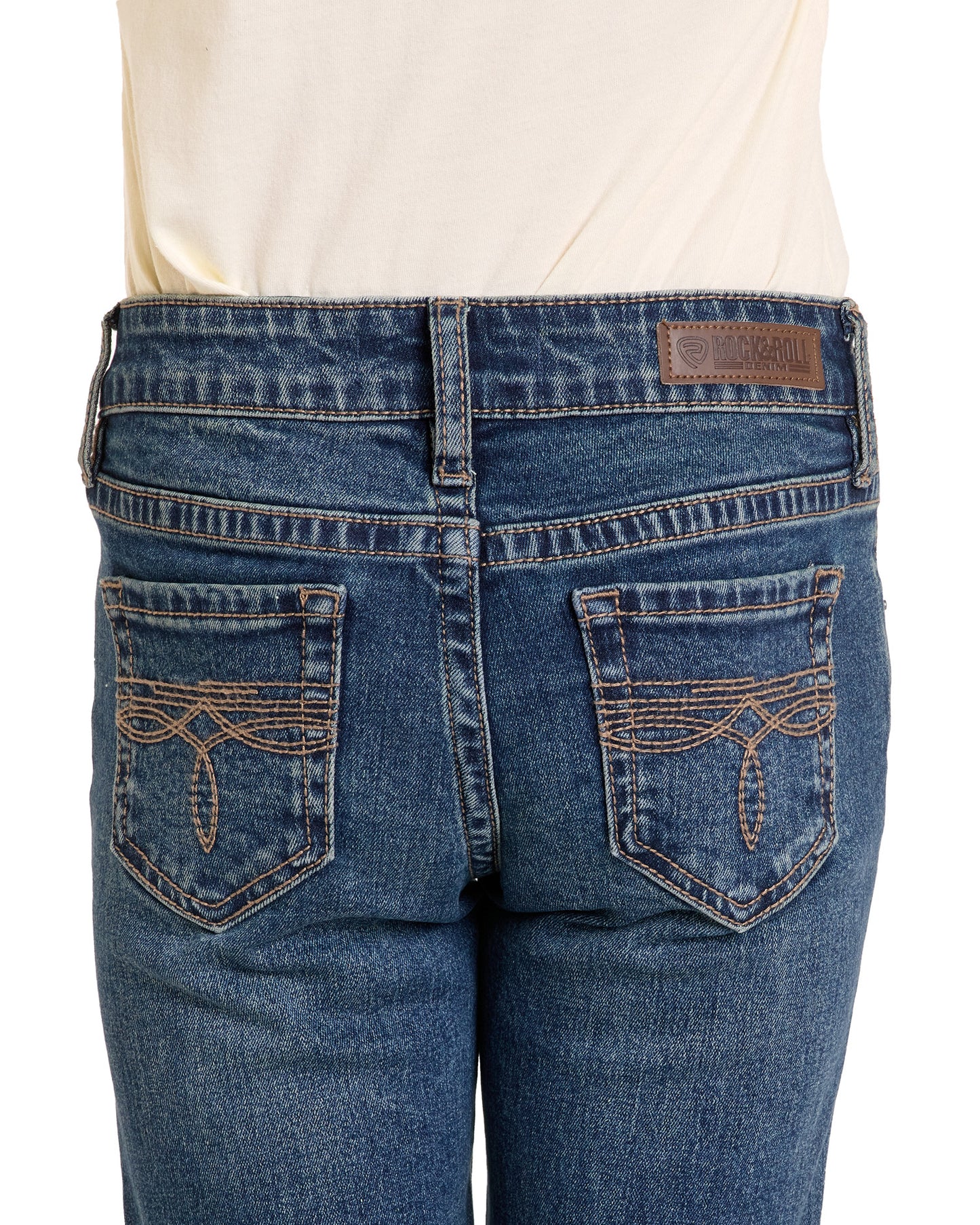 Close-up of Rock & Roll Denim Girls' Boot Stitch Bootcut Jeans, featuring decorative pocket stitching and a brown leather patch on the waistband, worn with a cream-colored shirt.