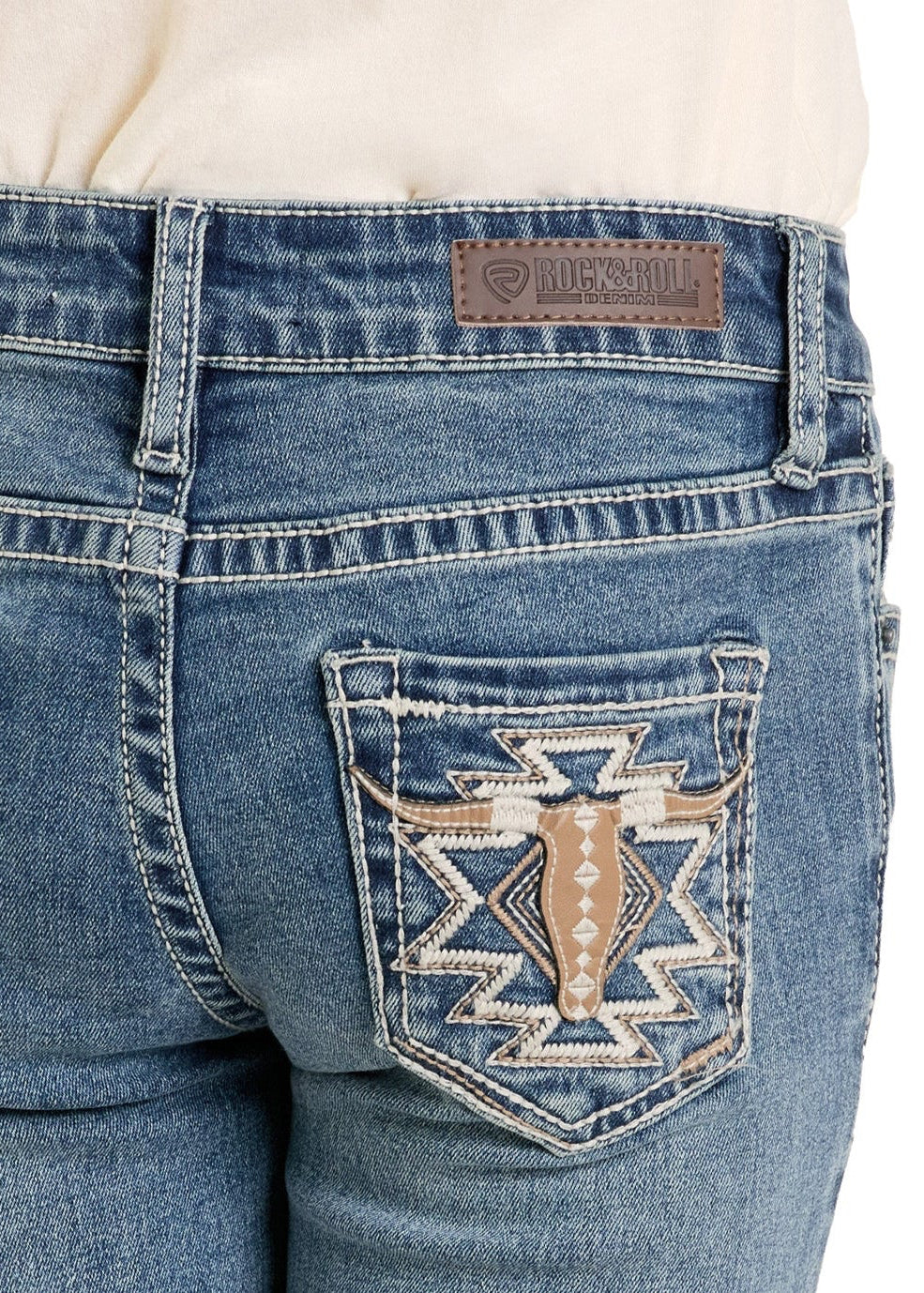 Close-up of the back of a person wearing Rock & Roll Denim Girls' Steer Pocket Bootcut Jeans, featuring decorative stitching, tan, white, and brown embroidery on the back pockets, and a brown leather patch on the waistband.