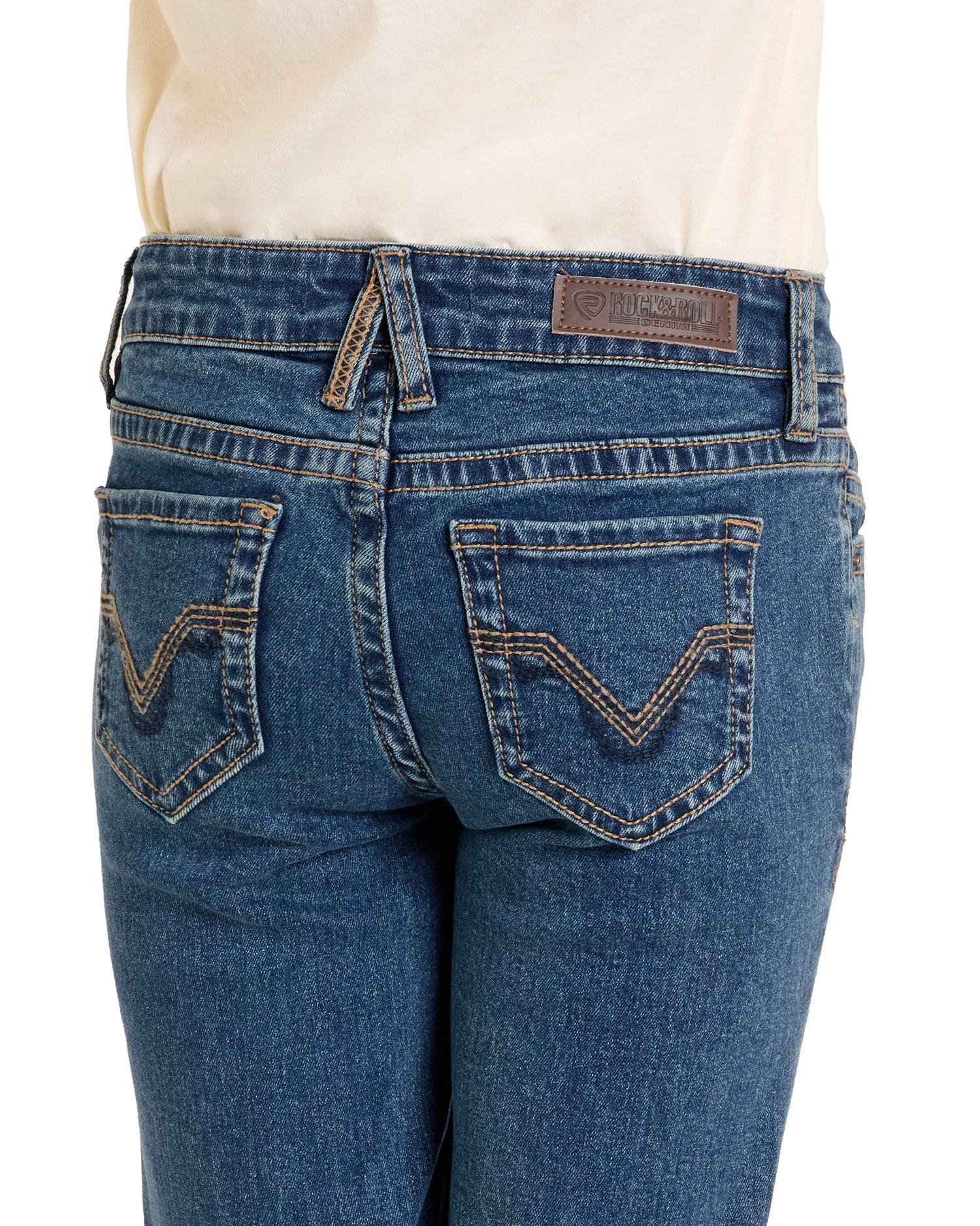 A close-up of the back of a girl wearing Rock & Roll Denim Girls' Signature Stitch Trouser Jeans in blue, featuring decorative back pocket stitching, a brown leather waistband patch, and a white top.