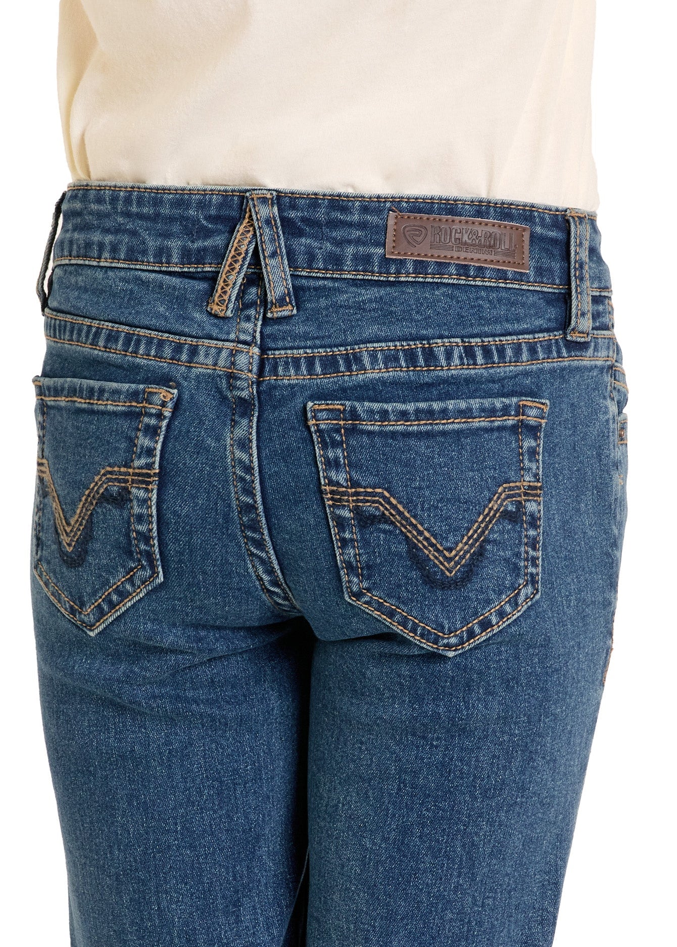 A close-up of the back of a girl wearing Rock & Roll Denim Girls' Signature Stitch Trouser Jeans in blue, featuring decorative back pocket stitching, a brown leather waistband patch, and a white top.