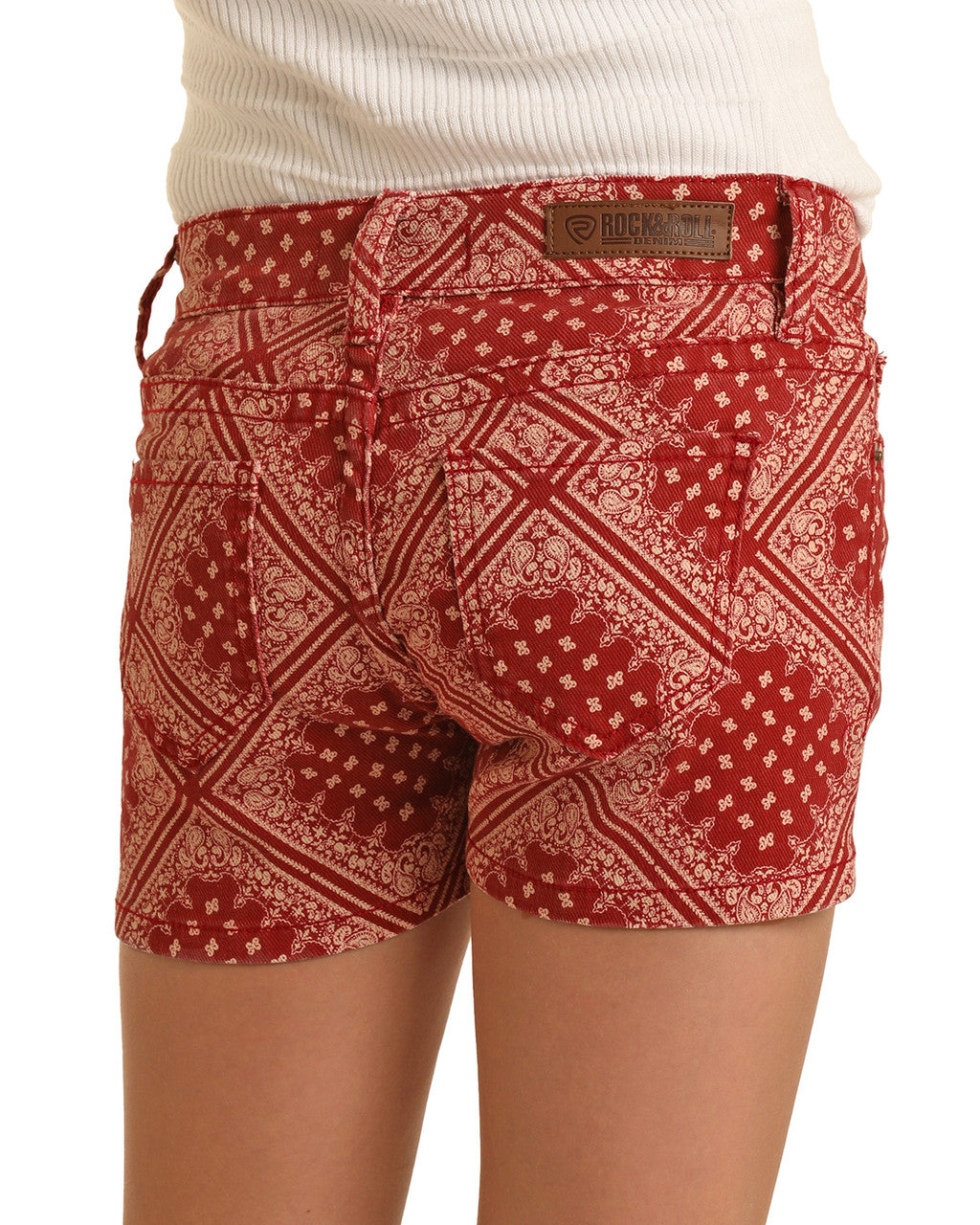 A person wearing Rock & Roll Denim Girls' Bandana Denim Shorts featuring western charm and a brown leather patch on the waistband, paired with a white ribbed top.