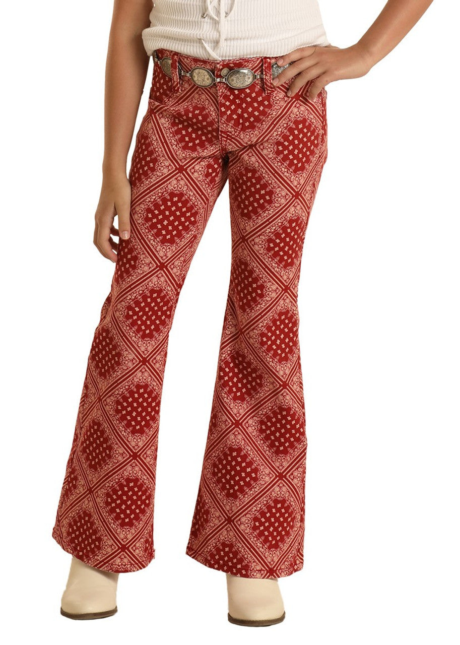A person dons Rock & Roll Denim Girls' Bandana Print Flare Jeans paired with a brown belt, white sleeveless top, and cream boots, striking a pose with one hand on their hip for a western-inspired style.