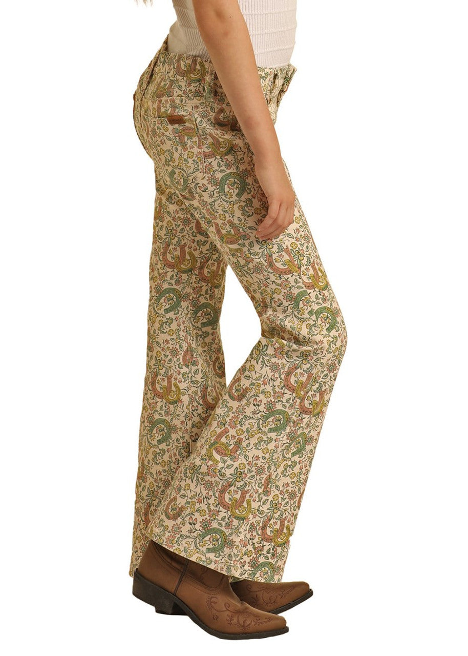 A person wears Rock & Roll Denim Girls' Floral Horseshoe Print Flare Jeans, brown cowboy boots, and a white ribbed top while standing in profile against a white background.