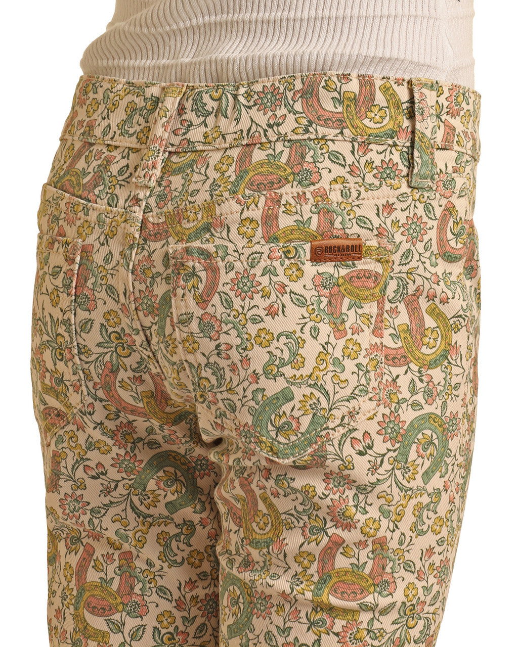A close-up of someone wearing Girls' Floral Horseshoe Print Flare Jeans by Rock & Roll Denim, featuring a cream-colored floral print. They pair the jeans with a ribbed cream top.