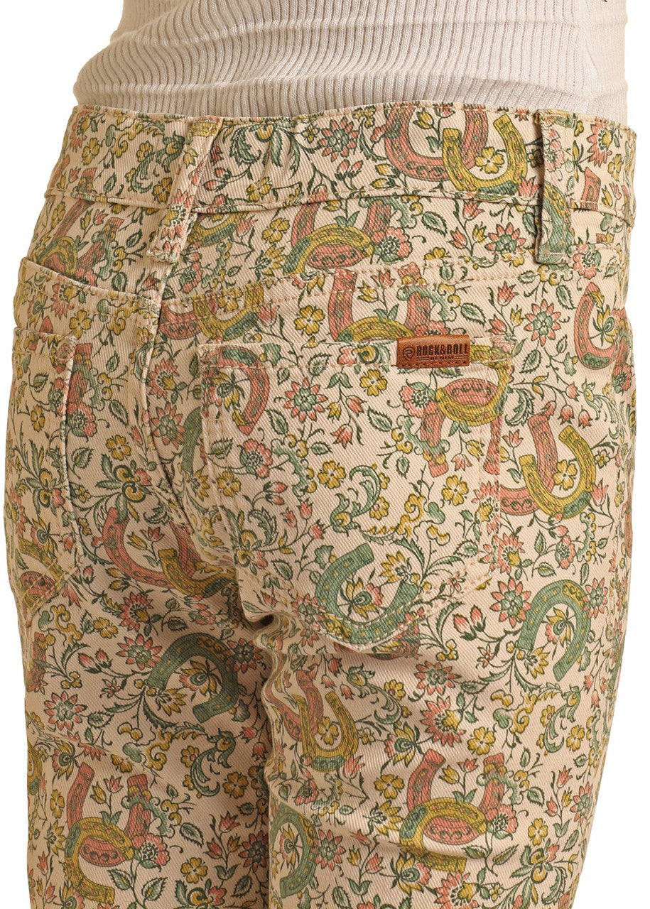A close-up of someone wearing Girls' Floral Horseshoe Print Flare Jeans by Rock & Roll Denim, featuring a cream-colored floral print. They pair the jeans with a ribbed cream top.