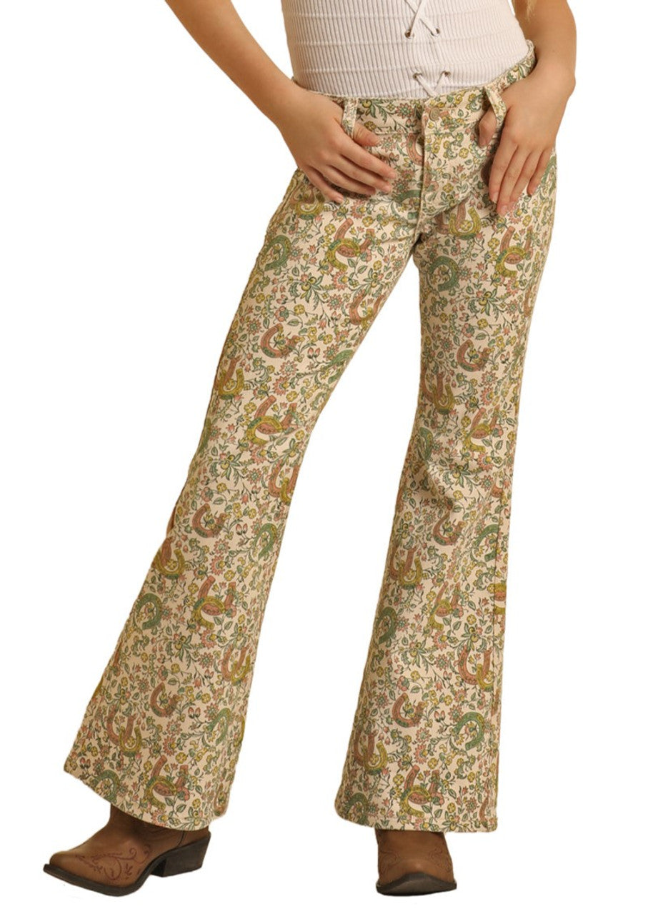 A person wearing Rock & Roll Denim Girls' Floral Horseshoe Print Flare Jeans, paired with a light top and brown heeled boots, stands with hands resting on their upper thighs.