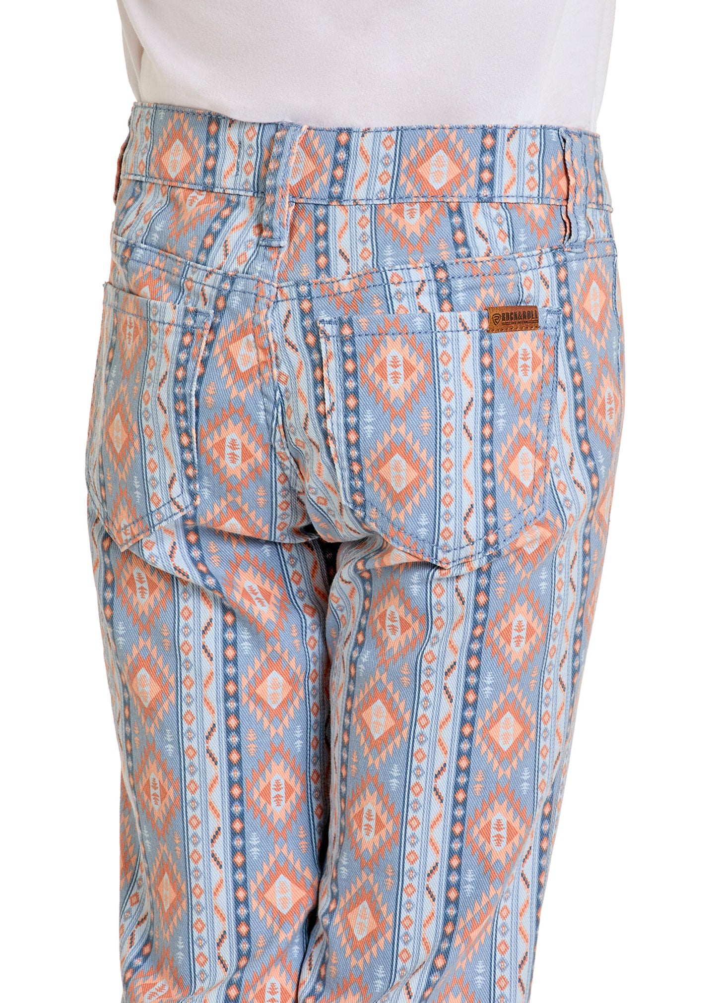 A person is wearing Rock & Roll Denim Girls' American Aztec Print Flare Jeans with a blue, orange, and white geometric pattern; image shows the back view with two pockets and a brown leather patch near the waistband.