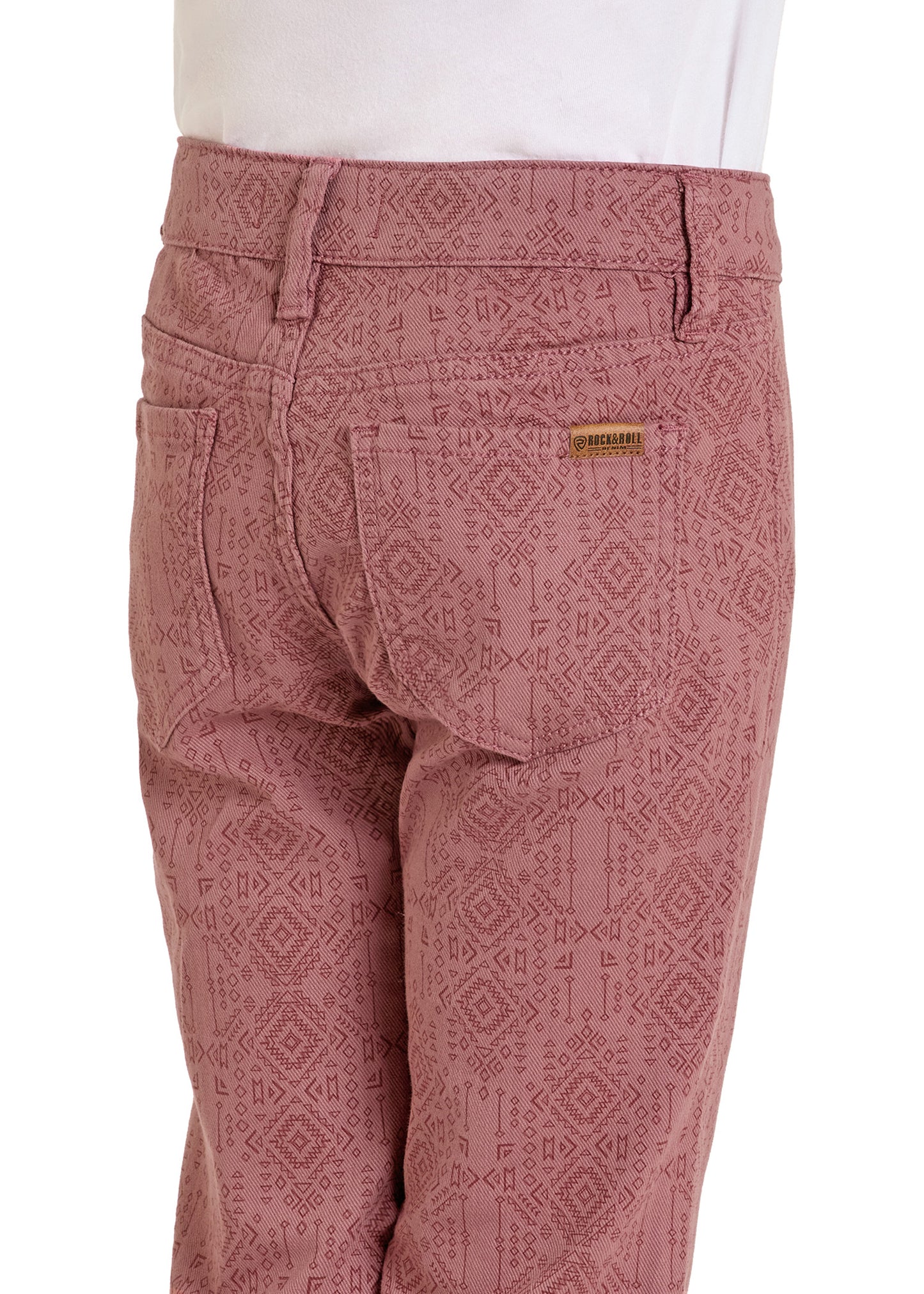 A person wearing Rock & Roll Denim Girls' Aztec Flare Jeans in dusty pink with a geometric pattern and back pockets, paired with a partially visible white shirt at the waist.