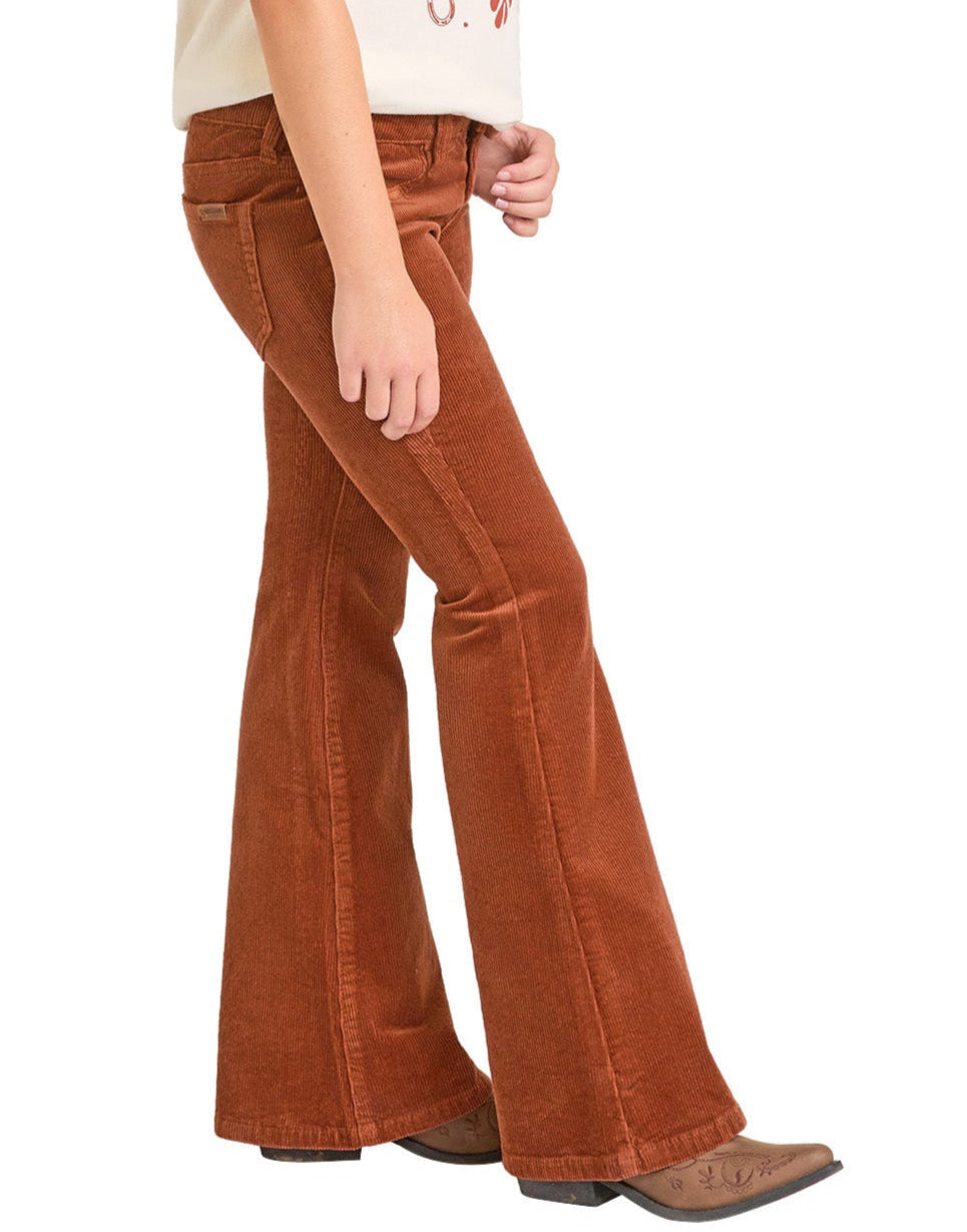 A person in Rock & Roll Denim Girls' Rust Corduroy Flare Jeans, a white shirt, and brown cowboy boots stands sideways against a white background, showcasing classic cowgirl style.
