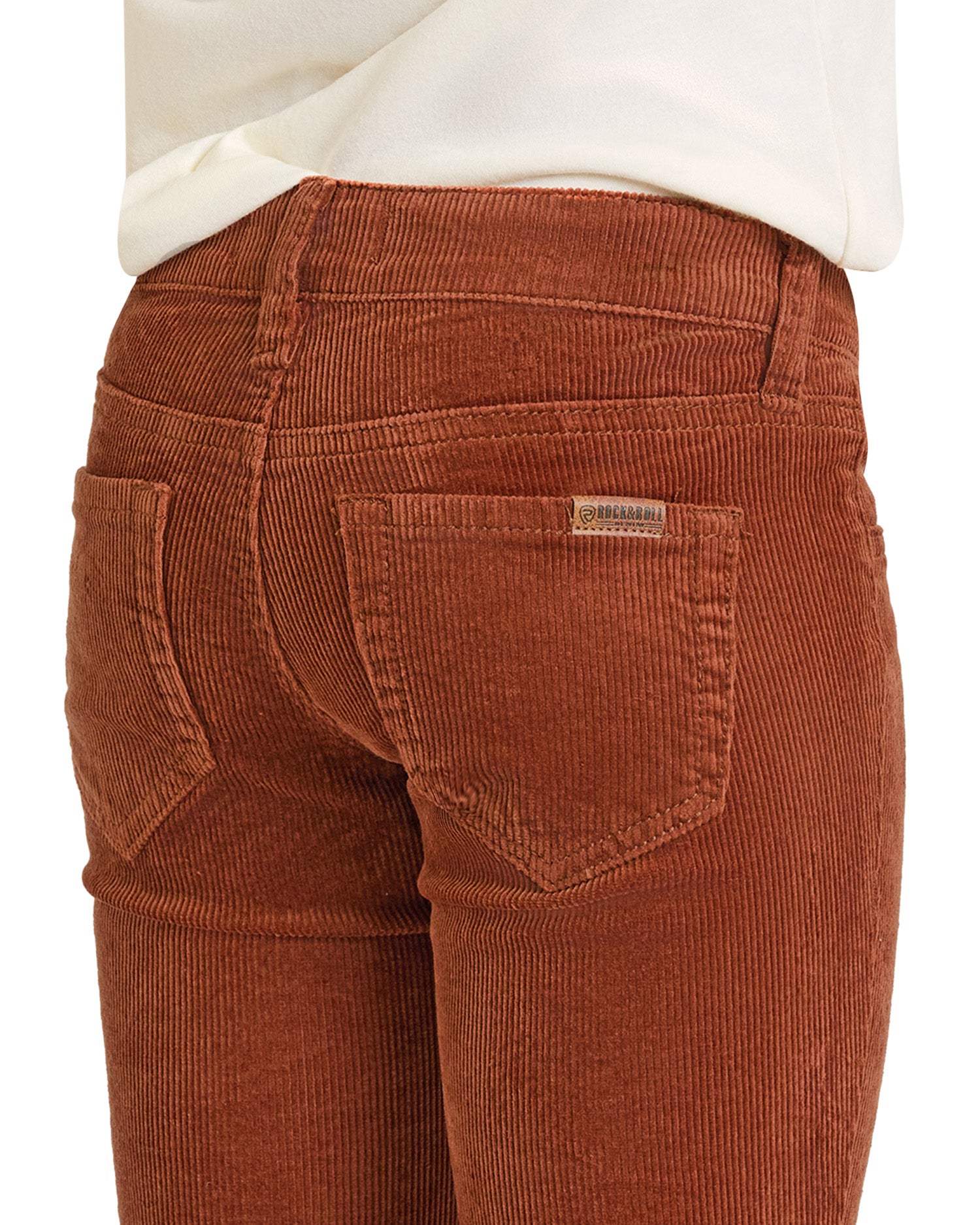 A close-up of a person wearing Rock & Roll Denim Girls' Rust Corduroy Flare Jeans with back pockets and a white shirt, showcasing the textured fabric, flattering fit, and subtle cowgirl style.