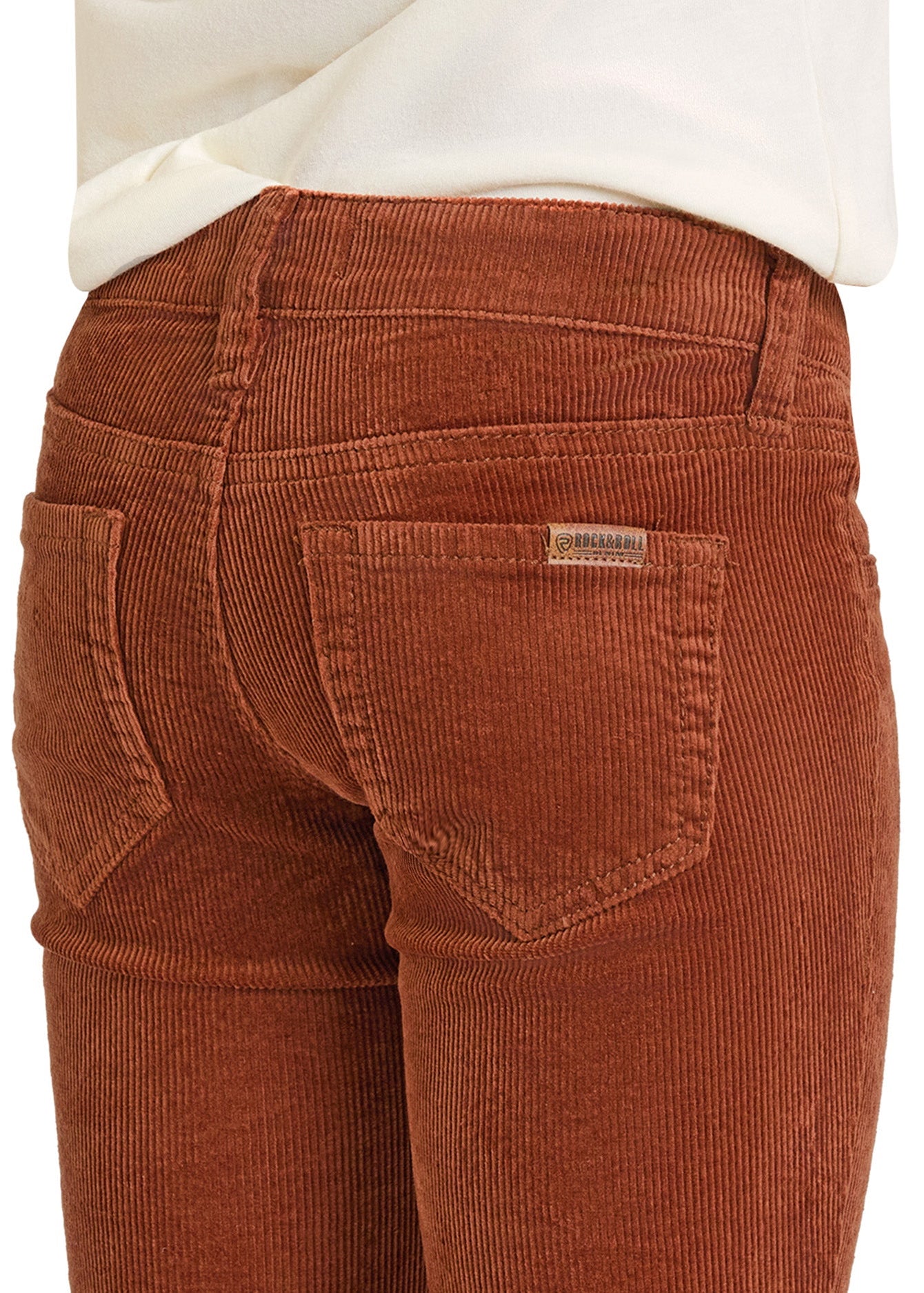 A close-up of a person wearing Rock & Roll Denim Girls' Rust Corduroy Flare Jeans with back pockets and a white shirt, showcasing the textured fabric, flattering fit, and subtle cowgirl style.