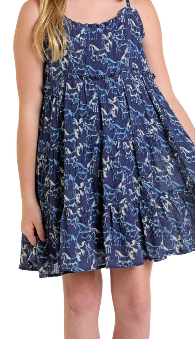 A young girl models the Rock & Roll Denim Girls' Horse Dress, a sleeveless navy blue outfit with a ruffled neckline and white and light blue horse pattern. Only her lower face, arms, and part of her legs are visible.