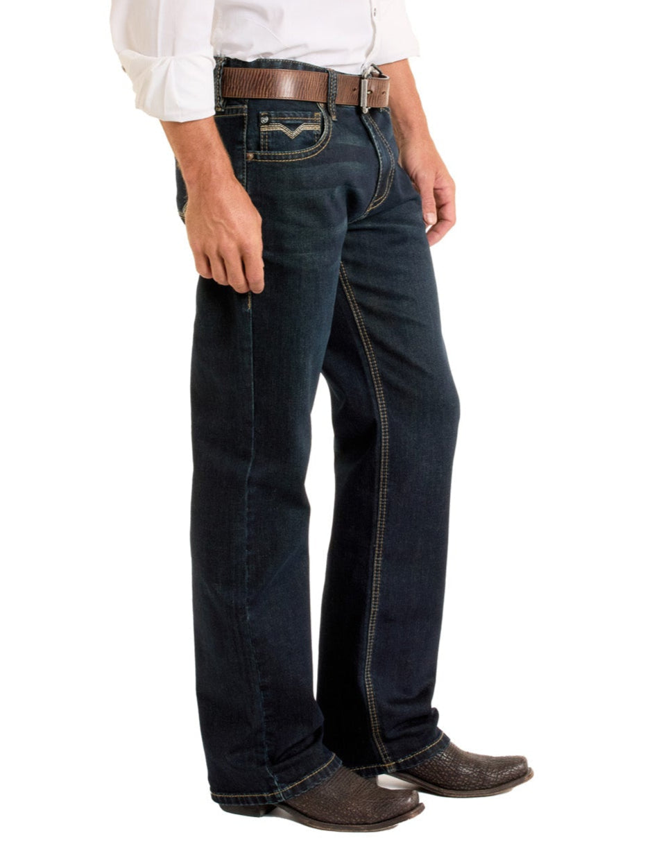 A man wearing Rock & Roll Denim Relaxed Fit Flat Seam Pocket Straight Leg Jeans, a white shirt, brown belt, and brown cowboy boots stands against a white background, with only the lower half of his body visible.