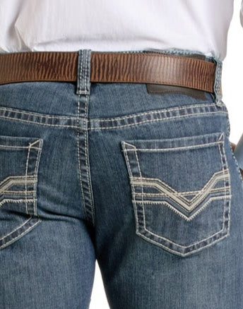 Close-up of a person wearing Rock & Roll Denim Slim Fit Embroidered Classic V Straight Leg Jeans with decorative back pocket stitching, a brown leather belt, and a white tucked-in shirt.