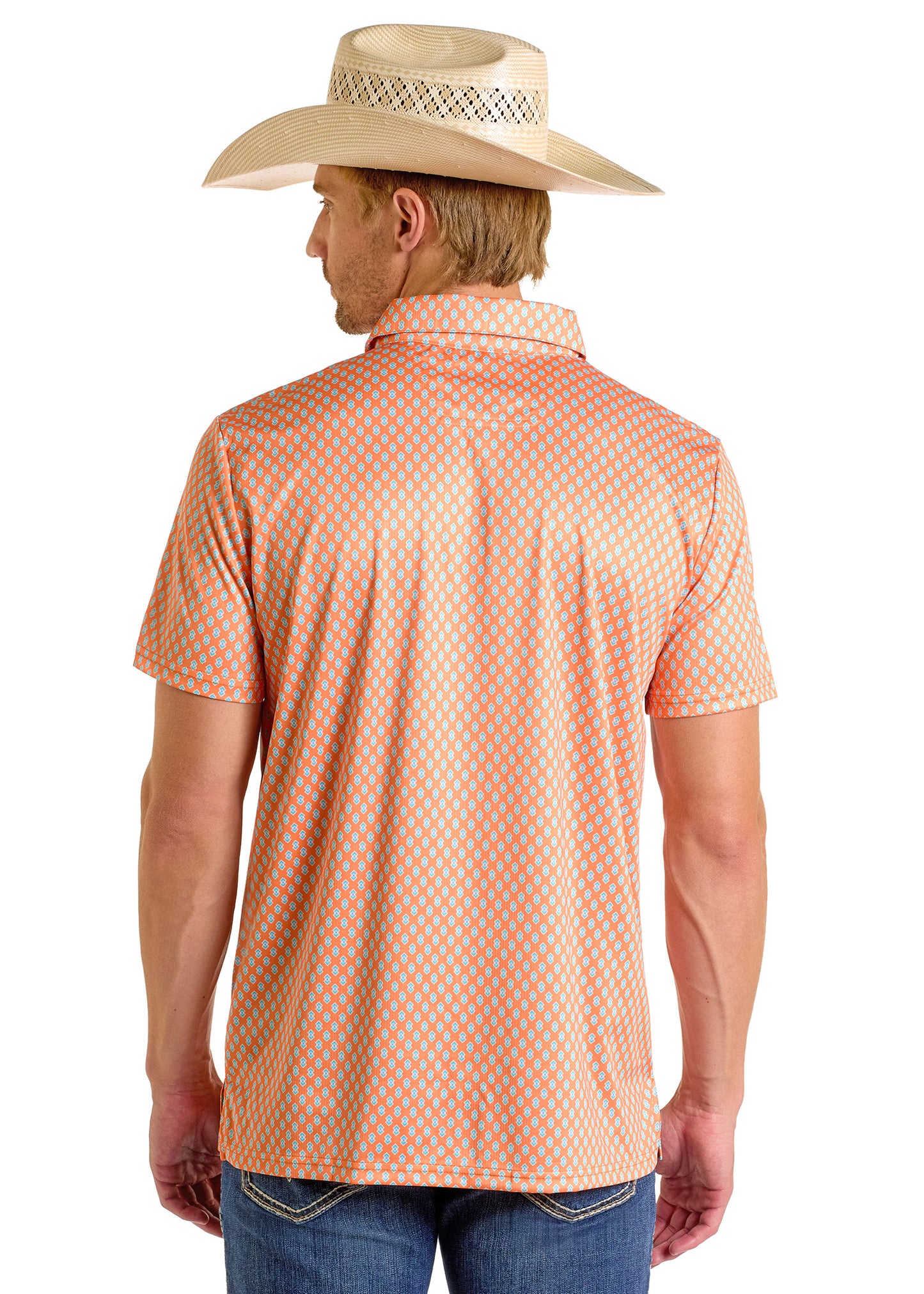 A man wearing a Rock & Roll Denim Geo Polo with an orange pattern, straw cowboy hat, and blue jeans stands with his back to the camera.
