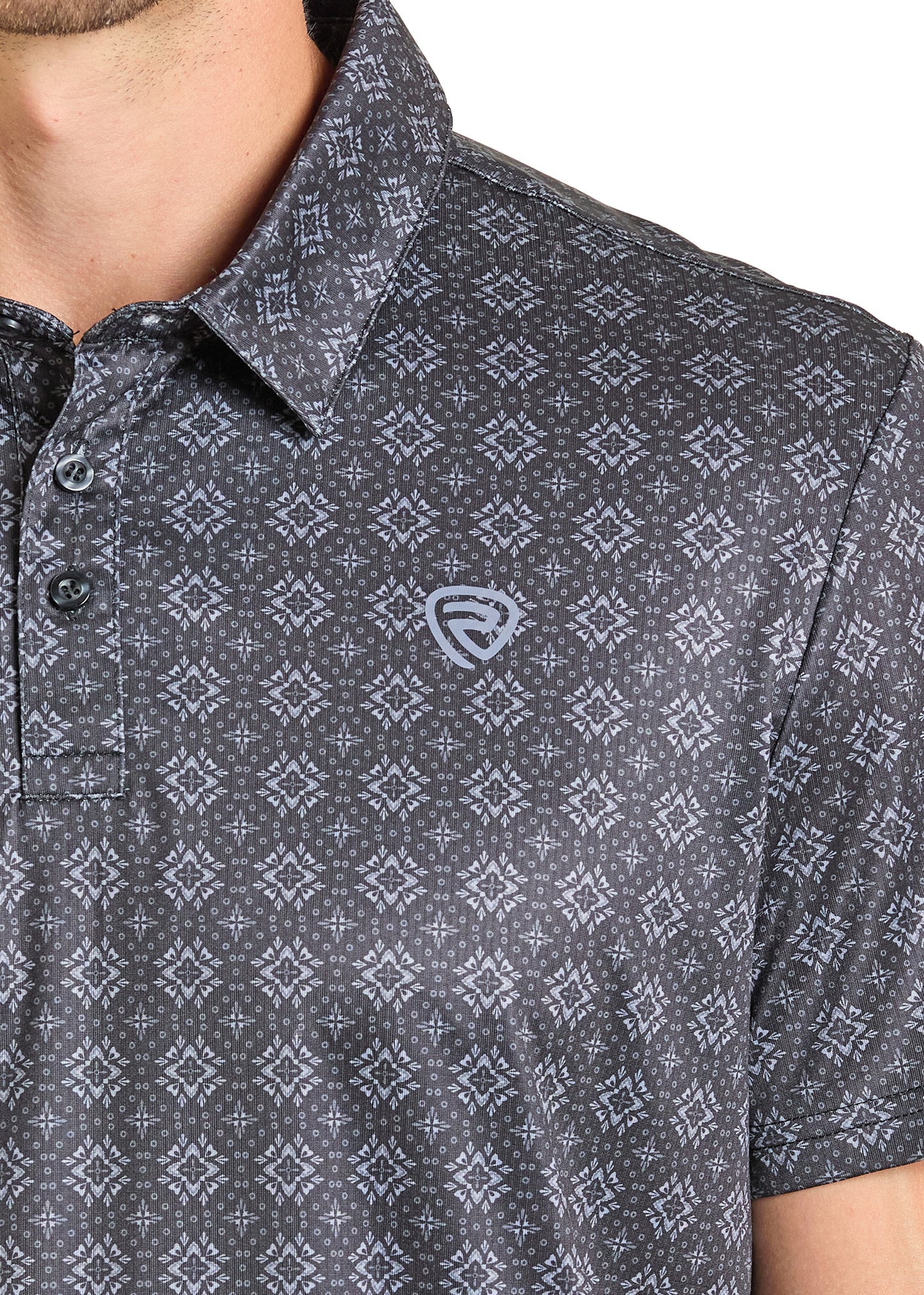 A close-up of a person wearing the Rock & Roll Denim Black Medallion Polo, featuring a dark pattern, buttoned collar, and small light logo on the chest. Only the lower face, neck, and upper torso are shown against a plain background.