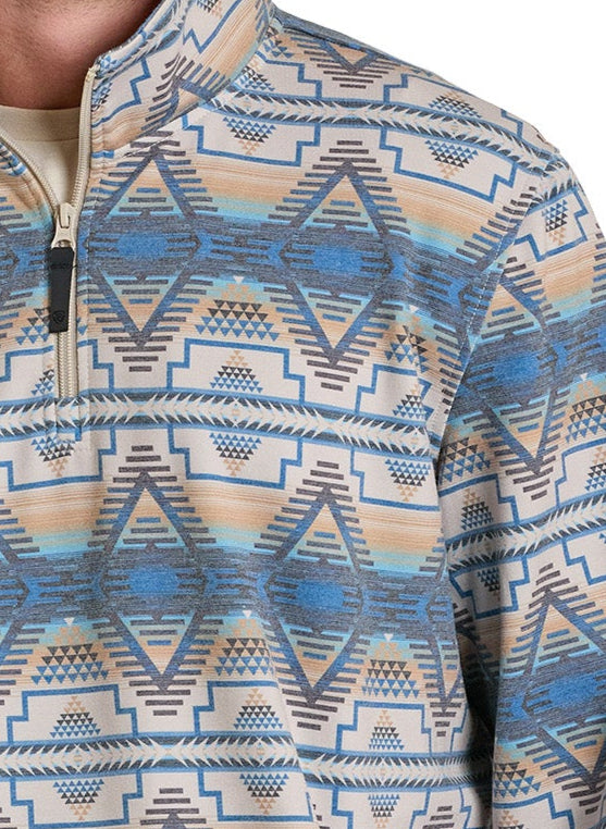 A close-up shows a person wearing the Rock & Roll Denim Aztec Print Performance Pullover in beige, blue, and gray with a bold geometric pattern. Only the upper torso and part of one arm are visible.