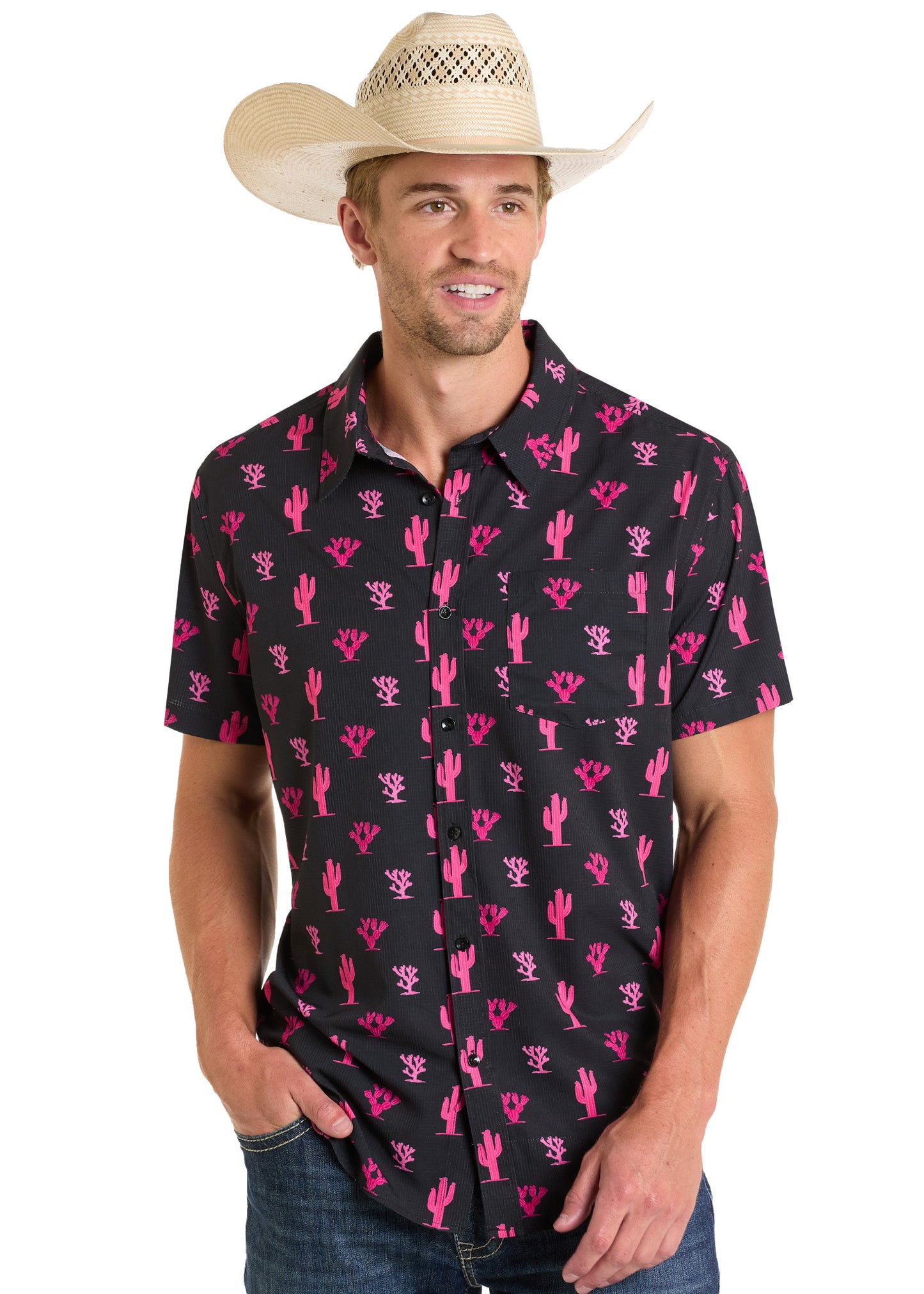 A man wearing a straw cowboy hat, blue jeans, and the Rock & Roll Denim TEK Western Pink Cactus Short Sleeve Shirt stands with one hand in his pocket, smiling.