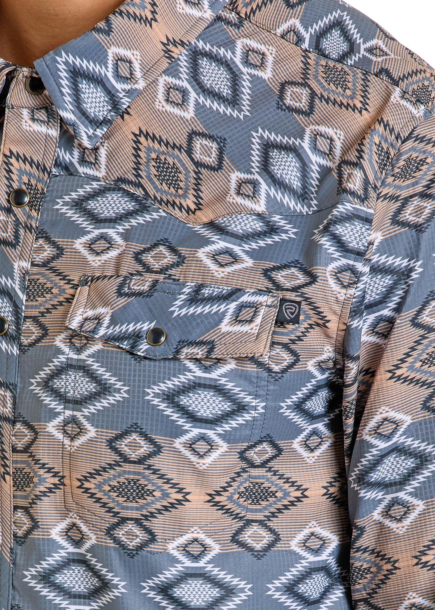 A close-up of the Rock & Roll Denim TEK Western Grey Aztec Long Sleeve Shirt, showcasing geometric patterns in brown, gray, and white. This button-up offers UPF 50 protection, a flap pocket with logo tag, and metal snap buttons.