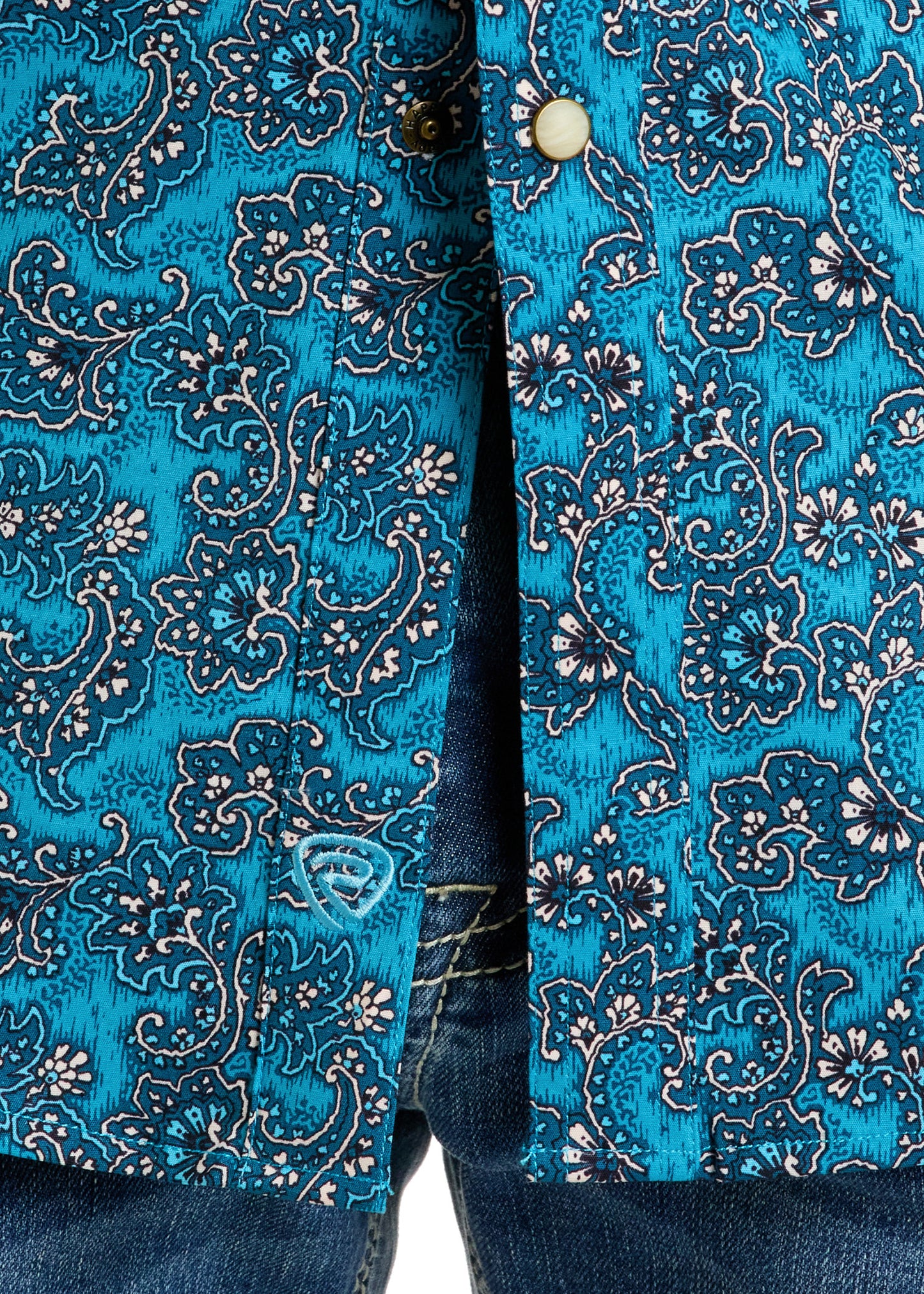 Close-up of the Rock & Roll Denim Slim Fit Turquoise Paisley Long Sleeve Snap Shirt (XL) with white floral designs, partially unbuttoned over blue denim jeans, highlighting the shirt’s detail and jeans’ waistband stitching.