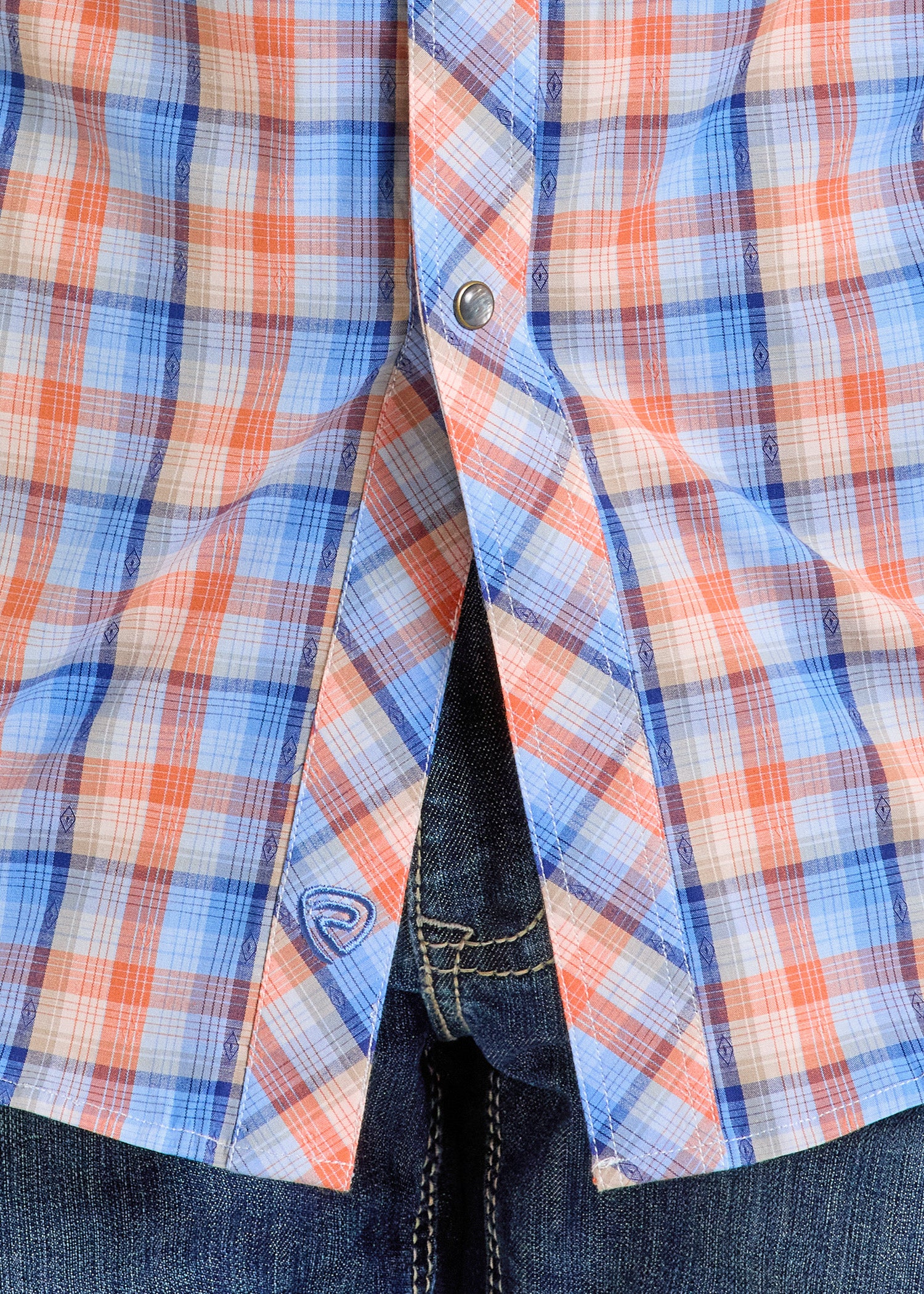 Close-up of a person in blue jeans and a Rock & Roll Denim Slim Fit Dobby Plaid Long Sleeve Snap Shirt - S, featuring blue, white, and red plaid pattern, with one snap button fastened and the shirt slightly open at the front.