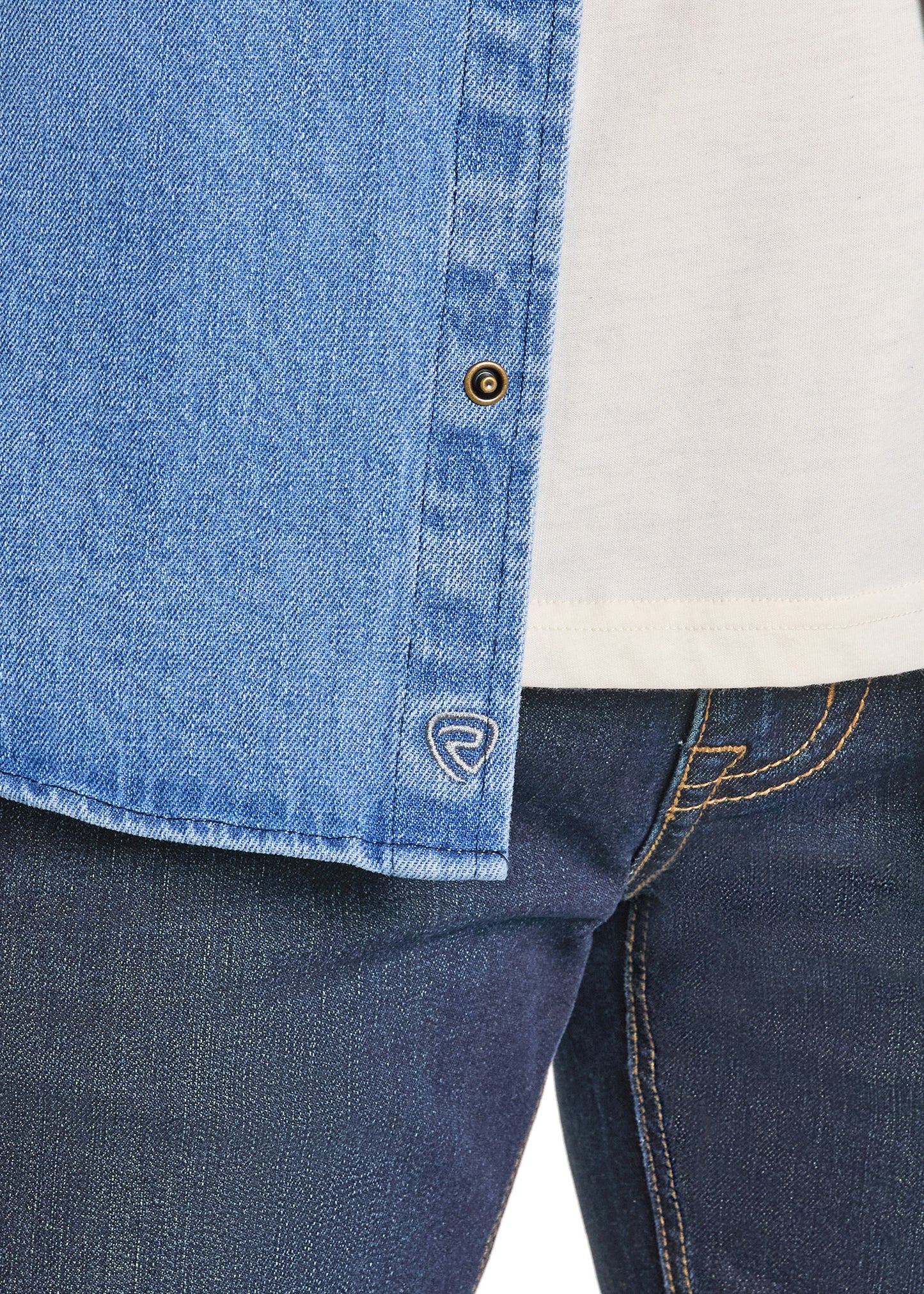 Close-up of a person wearing a blue denim shirt and jeans with a brand logo on the shirt.