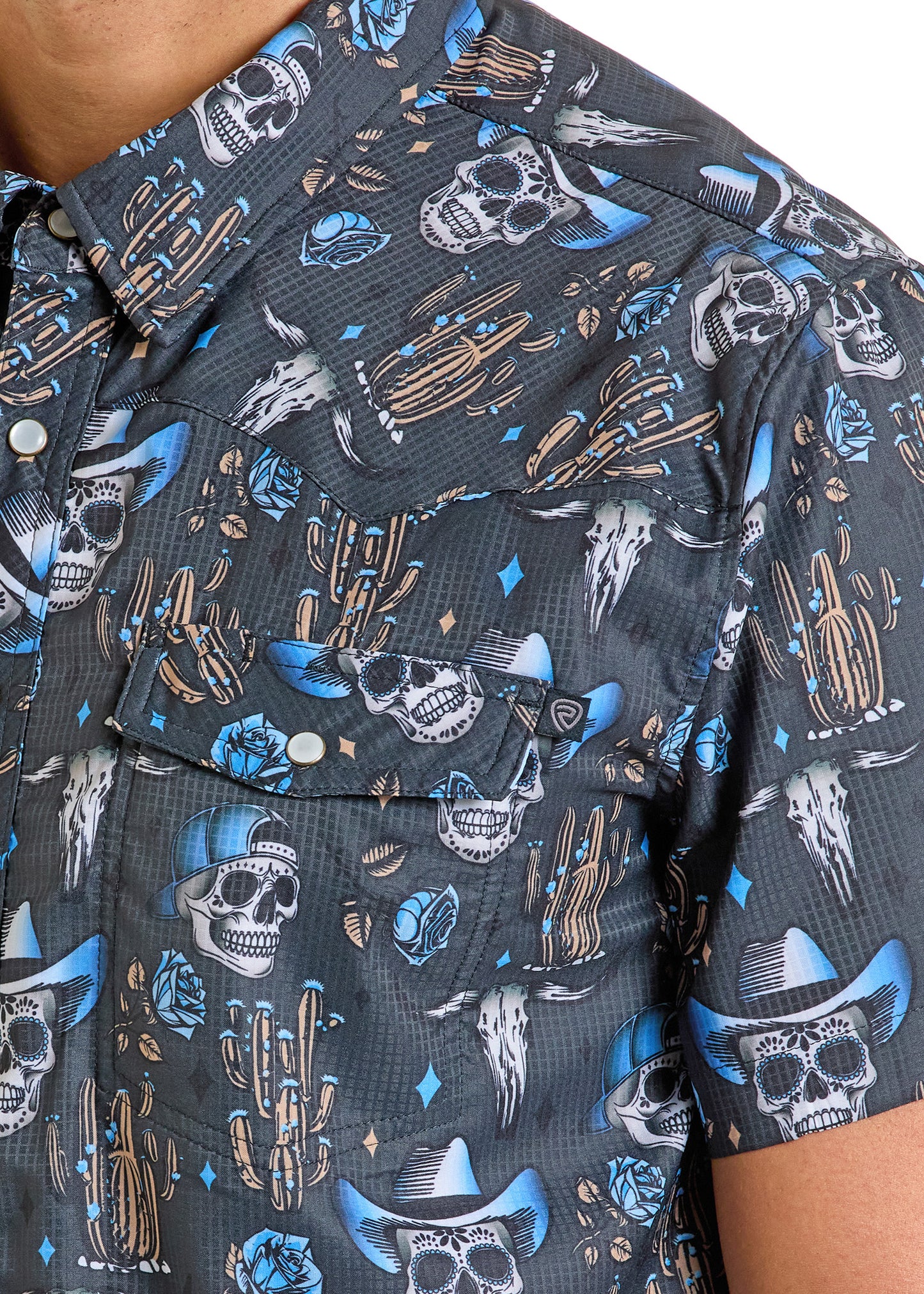 A close-up of a person wearing the Rock & Roll Denim TEK Western Skull Short Sleeve Shirt, featuring colorful cowboy hat skulls, cacti, roses, and diamonds on dark fabric with moisture-wicking comfort.
