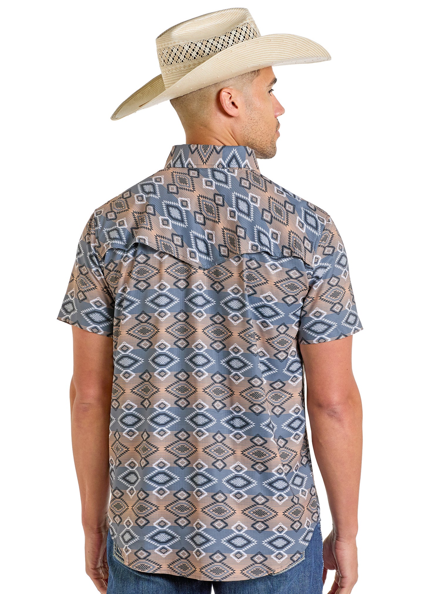 A man in a straw cowboy hat wears the Rock & Roll Denim TEK Western Bold Aztec Short Sleeve Shirt, featuring moisture-wicking fabric, and stands facing away to showcase the shirt’s back design.