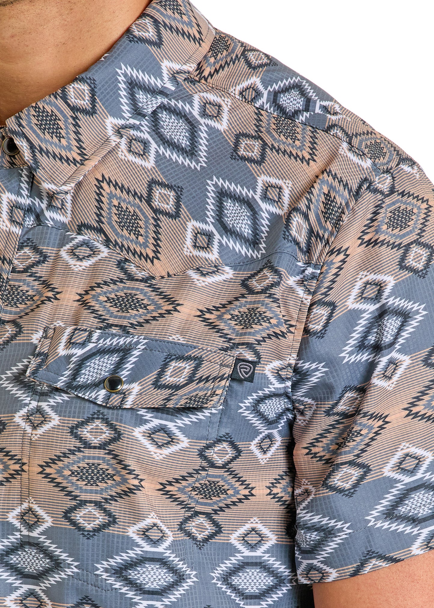 Close-up of a person wearing the Rock & Roll Denim TEK Western Bold Aztec Short Sleeve Shirt, featuring a blue, beige, and white geometric diamond pattern, moisture-wicking fabric, and a buttoned chest pocket.