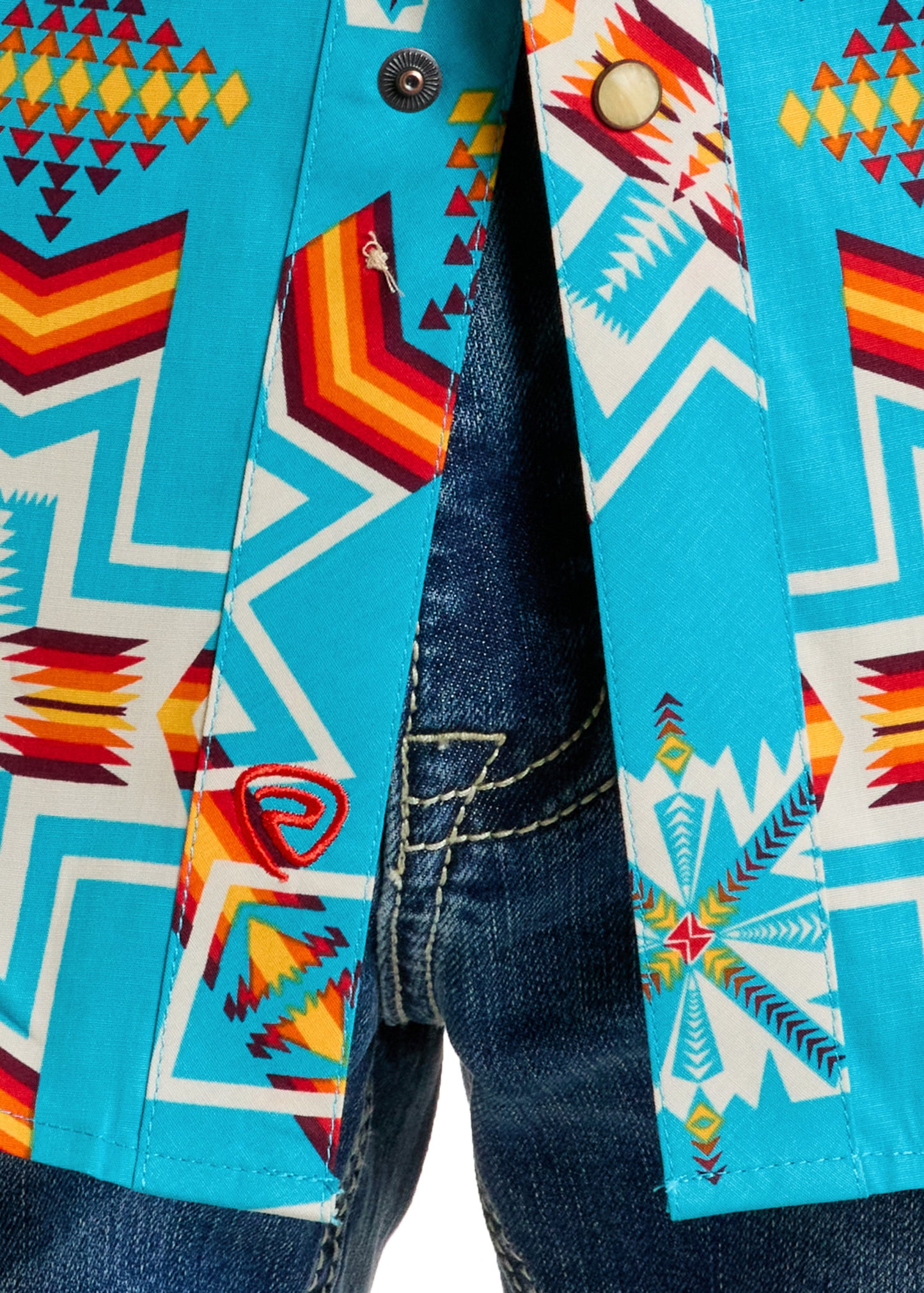 Close-up of a person wearing blue denim jeans and the Rock & Roll Denim Slim Fit Turquoise Aztec Short Sleeve Snap Shirt, which features colorful geometric tribal patterns and two metallic snaps on the front.