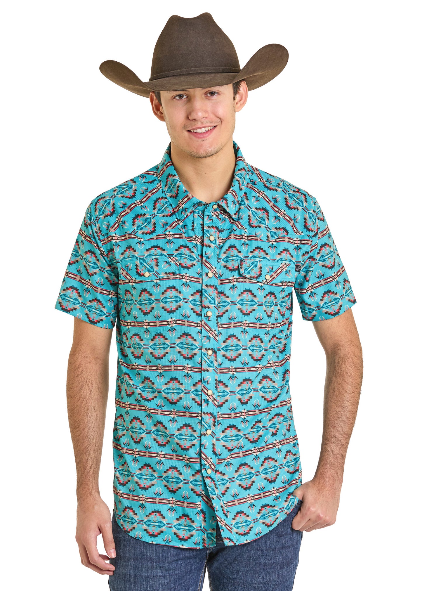 A young man wears a brown cowboy hat, Rock & Roll Denim's TEK Western Daring Aztec Short Sleeve Shirt with UPF 50 and a geometric pattern, and blue jeans, while standing and smiling at the camera.