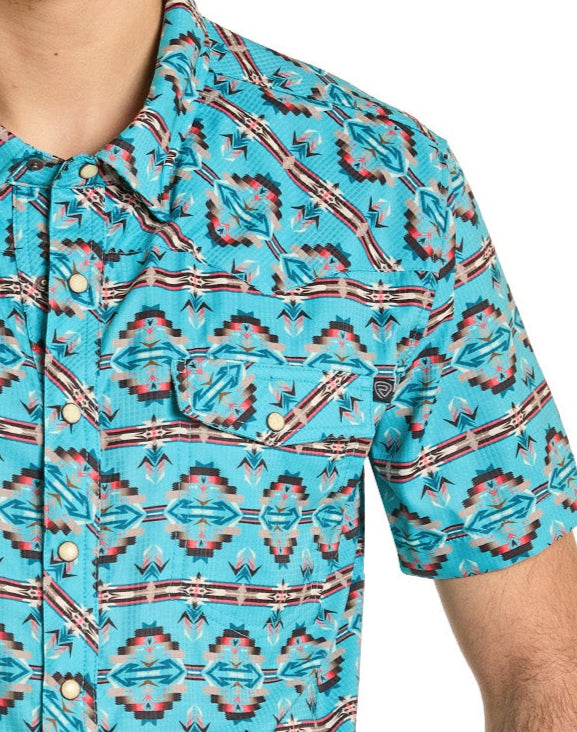 A person wearing the Rock & Roll Denim TEK Western Daring Aztec Short Sleeve Shirt, featuring a southwestern geometric pattern in turquoise, red, white, and black. Only the upper torso and part of one arm are visible.