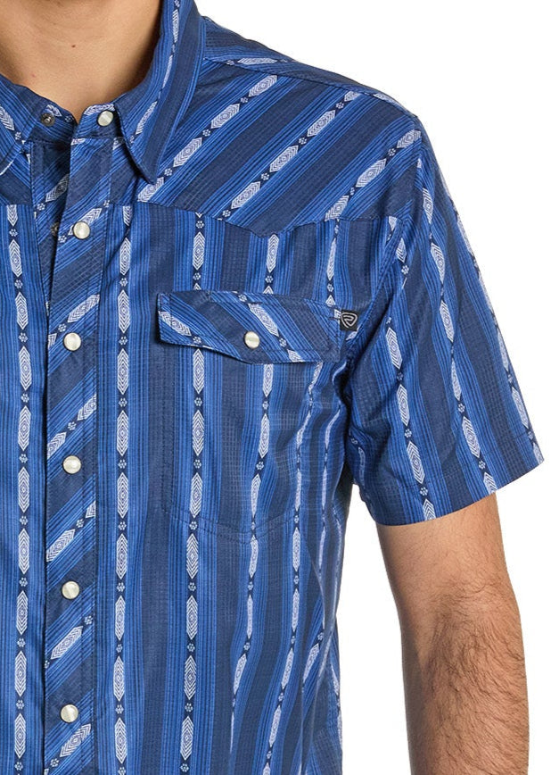 A person wears the Rock & Roll Denim TEK Western Vertical Print Short Sleeve Shirt in blue, showcasing a geometric white and navy stripe pattern, buttoned chest pocket, and moisture-wicking fabric. Only their upper body is visible.