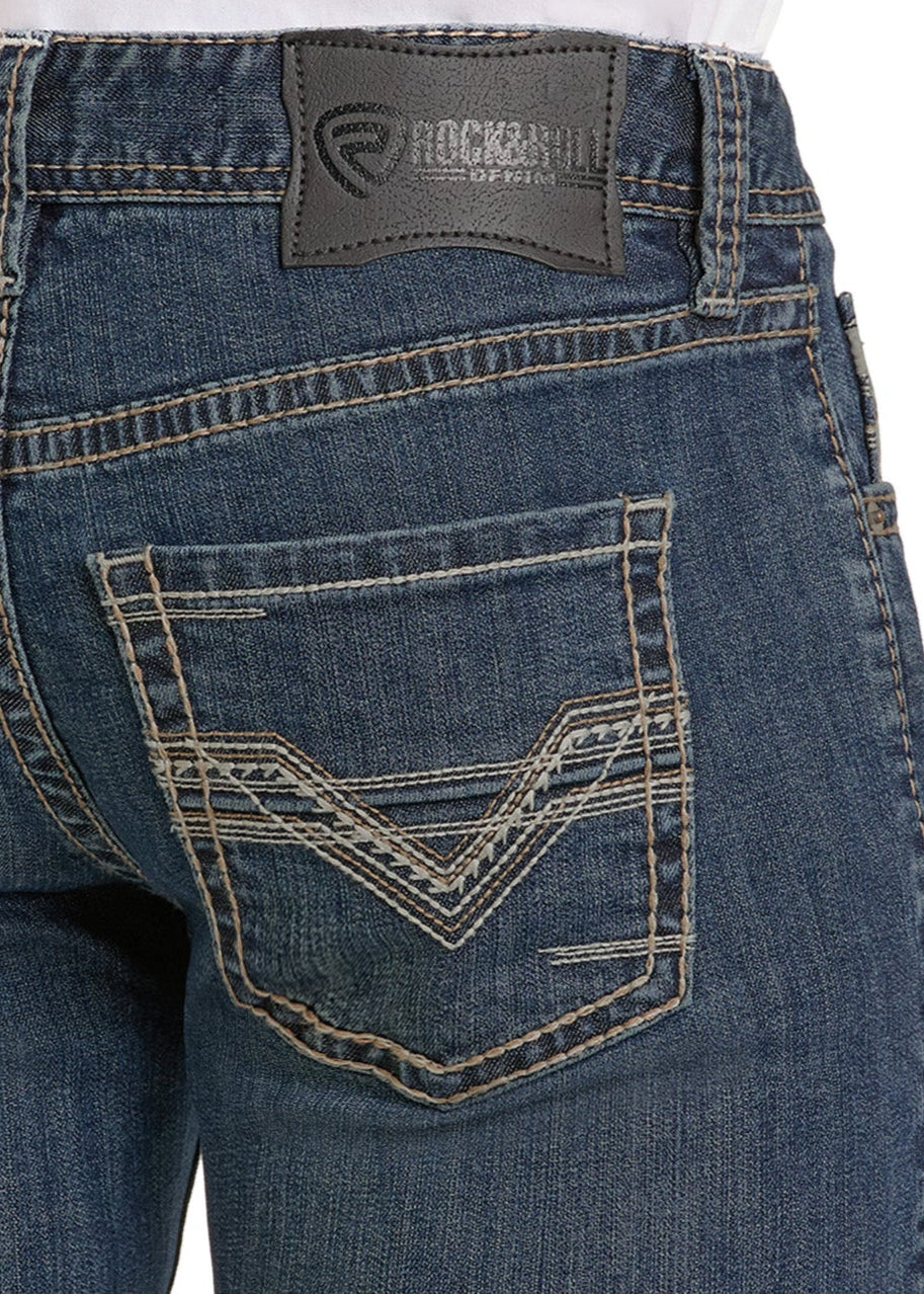 Close-up of the back of blue denim Regular Fit Ladder Stackable Bootcut Jeans by Rock & Roll Denim, featuring a brown leather brand patch above a back pocket with decorative light stitching.