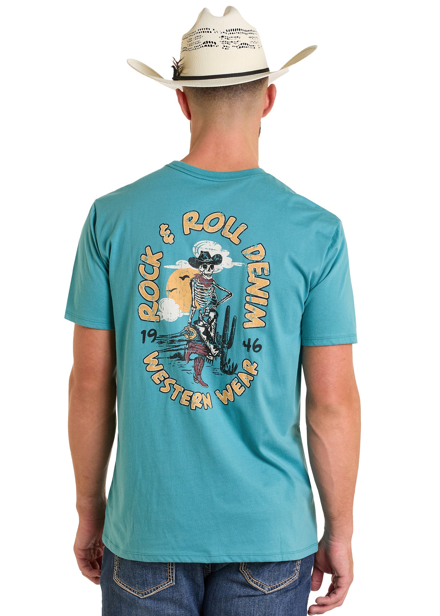 A man in a cowboy hat and jeans wears the Cowboy Skeleton Graphic Tee by Rock & Roll Denim, featuring cacti and a sunset. This comfy tee is perfect for everyday wear and has the brand's Western Wear text on the back.