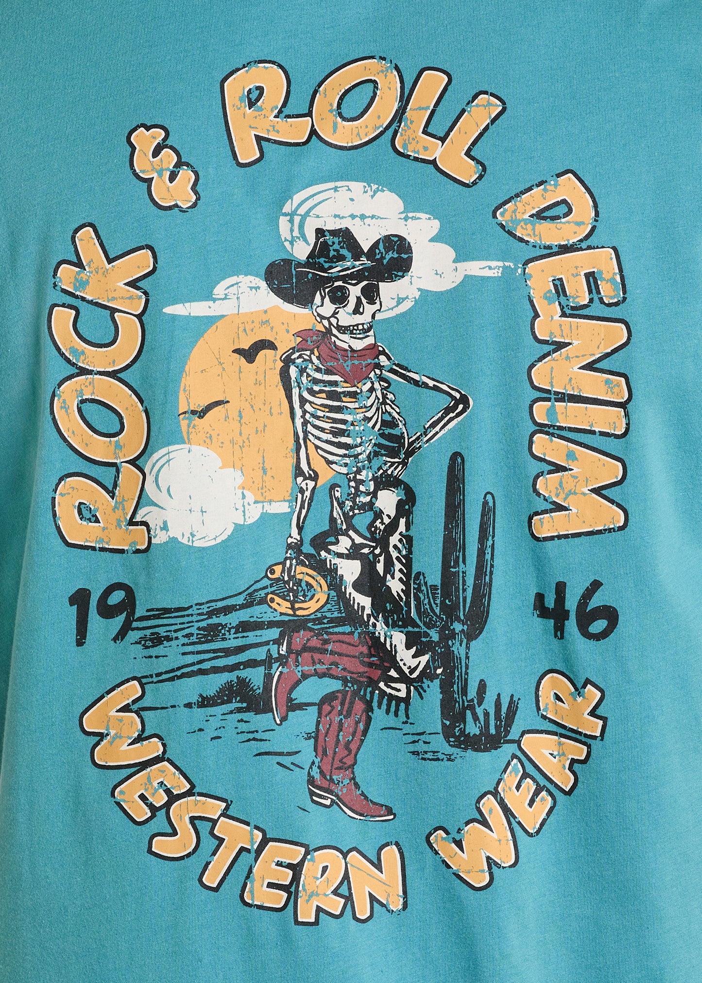 The Rock & Roll Denim Cowboy Skeleton Graphic Tee features a skeleton in cowboy gear by a cactus, yellow sun, and clouds on a teal background, with "Western Wear 1946"—a comfortable pick for everyday style.