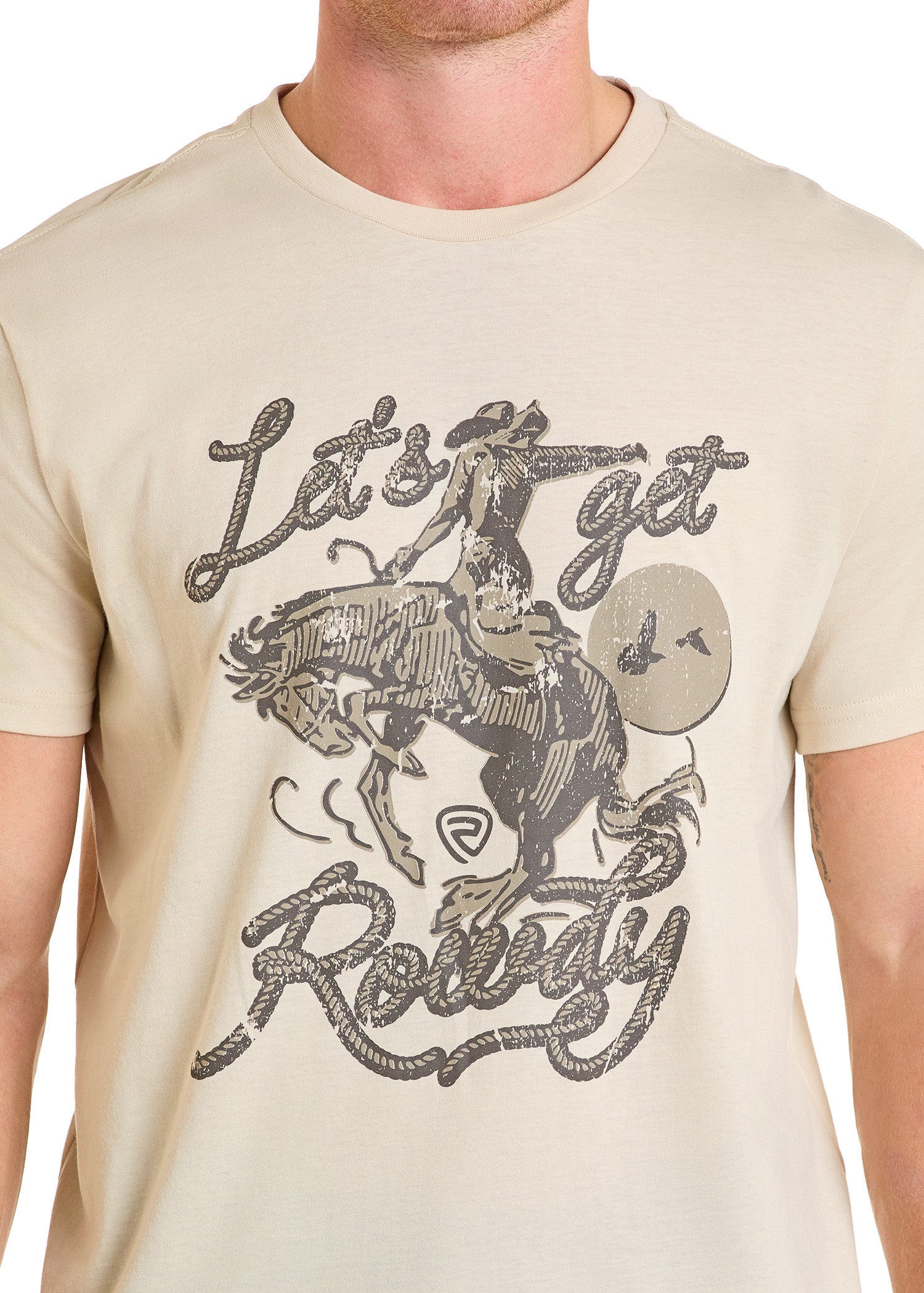 A person in the Rock & Roll Denim Let's Get Rowdy Graphic Tee—a beige shirt with a cowboy and bold text—enjoys comfy, everyday style.