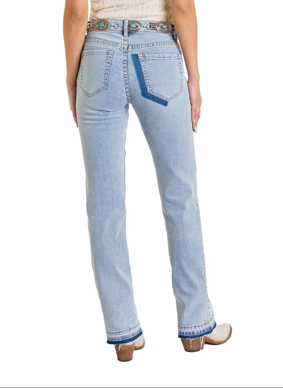 A person wearing Rock & Roll Denim's Mid Rise Distressed Two-Tone Modest Bootcut Jeans, featuring contrasting blue accents on the back pocket and hem, styled with a decorative belt and heeled shoes, shown from the back.