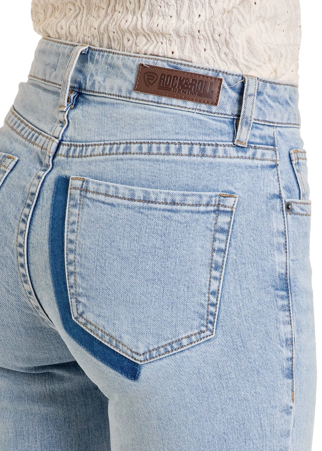 A person wears the Rock & Roll Denim Mid Rise Distressed Two-Tone Modest Bootcut Jeans, featuring a dark blue stripe on the back pocket, brown leather brand patch on the waistband, and pairs them with a textured white top.