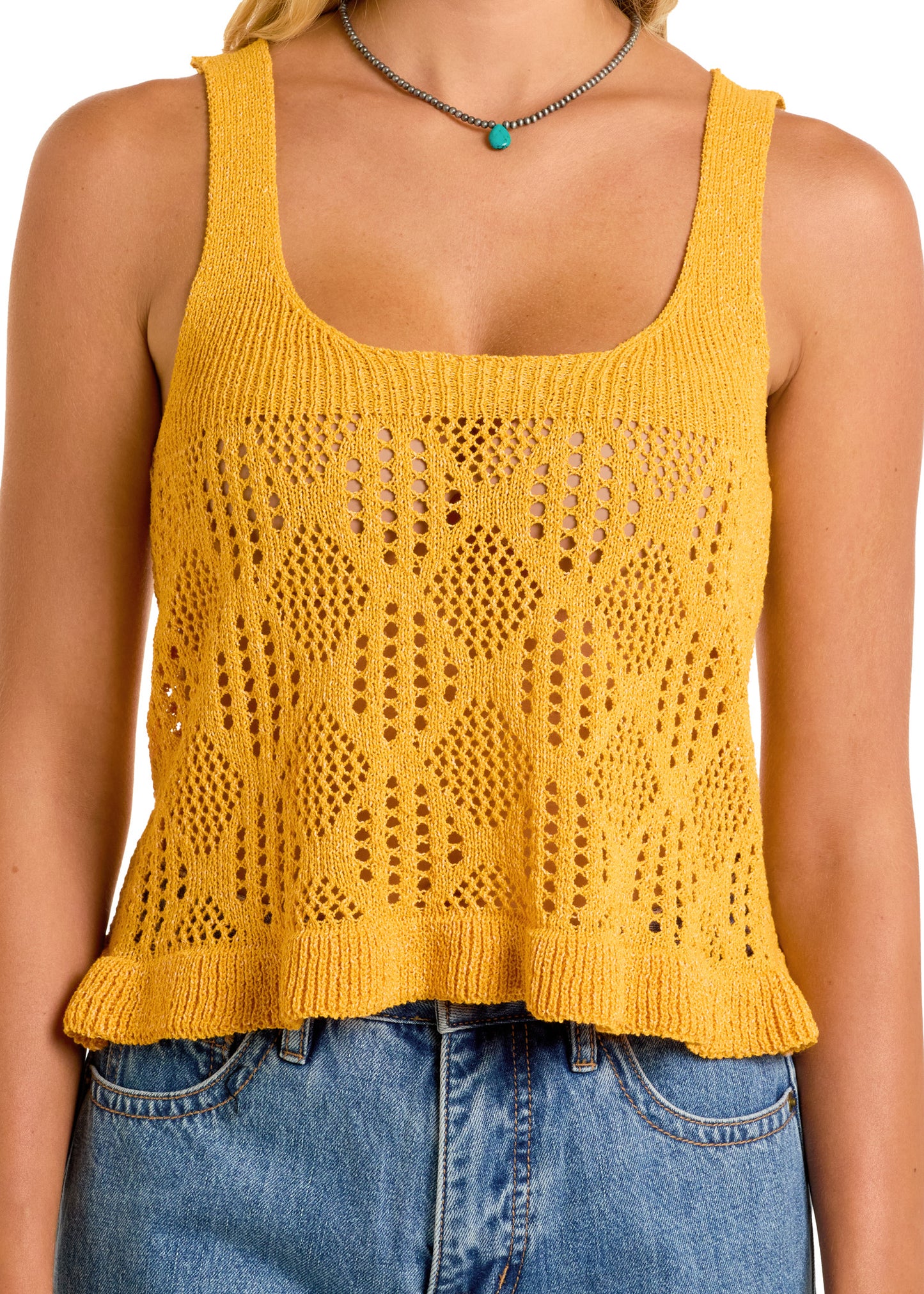 A woman wears a yellow Loose Knit Tank Top by Rock & Roll Denim with a diamond pattern, ruffled hem, and blue denim jeans. She accessorizes with a turquoise pendant necklace. The photo is cropped at the shoulders and waist.
