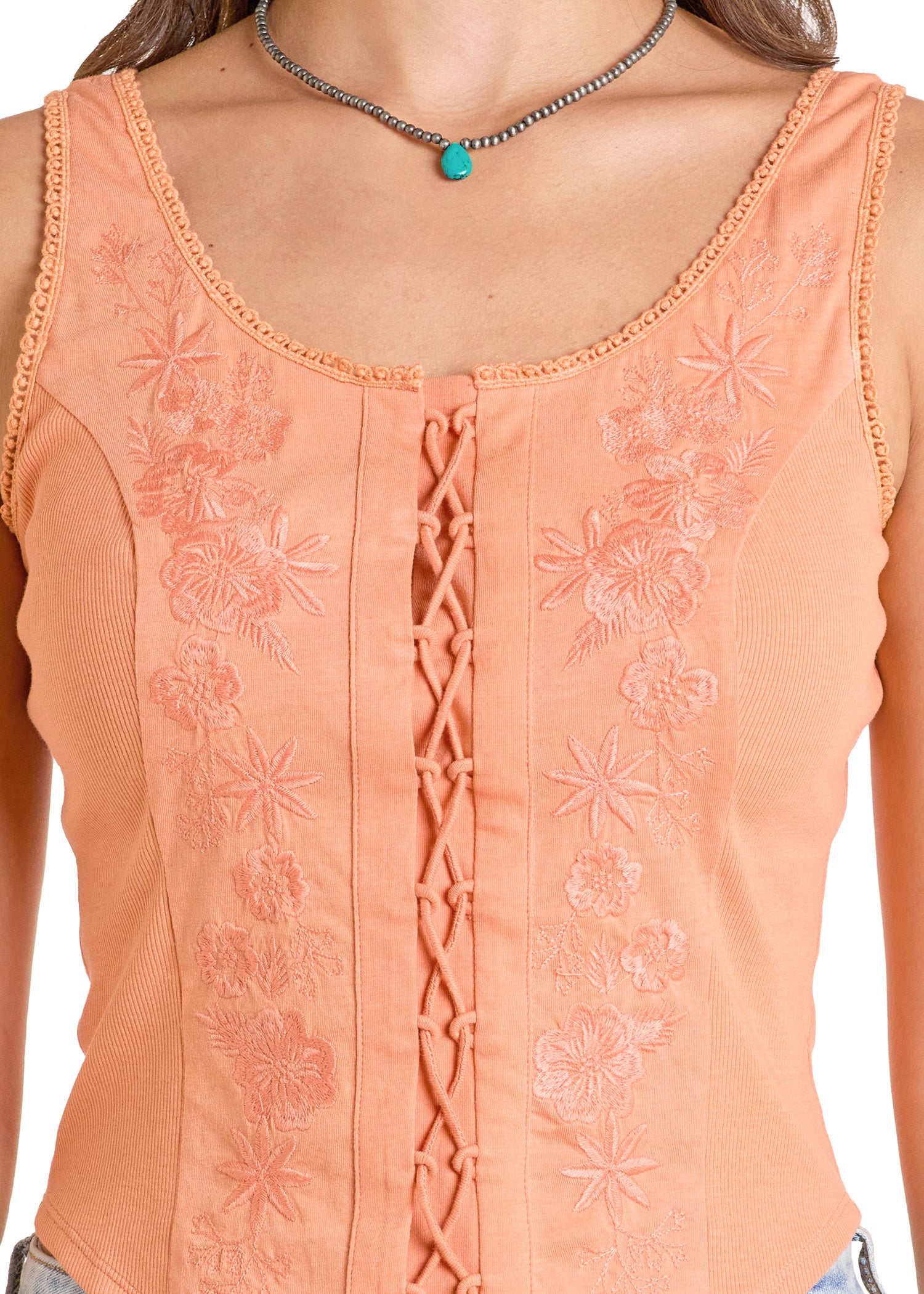 A close-up of a person wearing the Rock & Roll Denim Embroidered Lace-Up Tank with a fitted bodice and floral embroidery, paired with a silver necklace featuring a turquoise pendant.