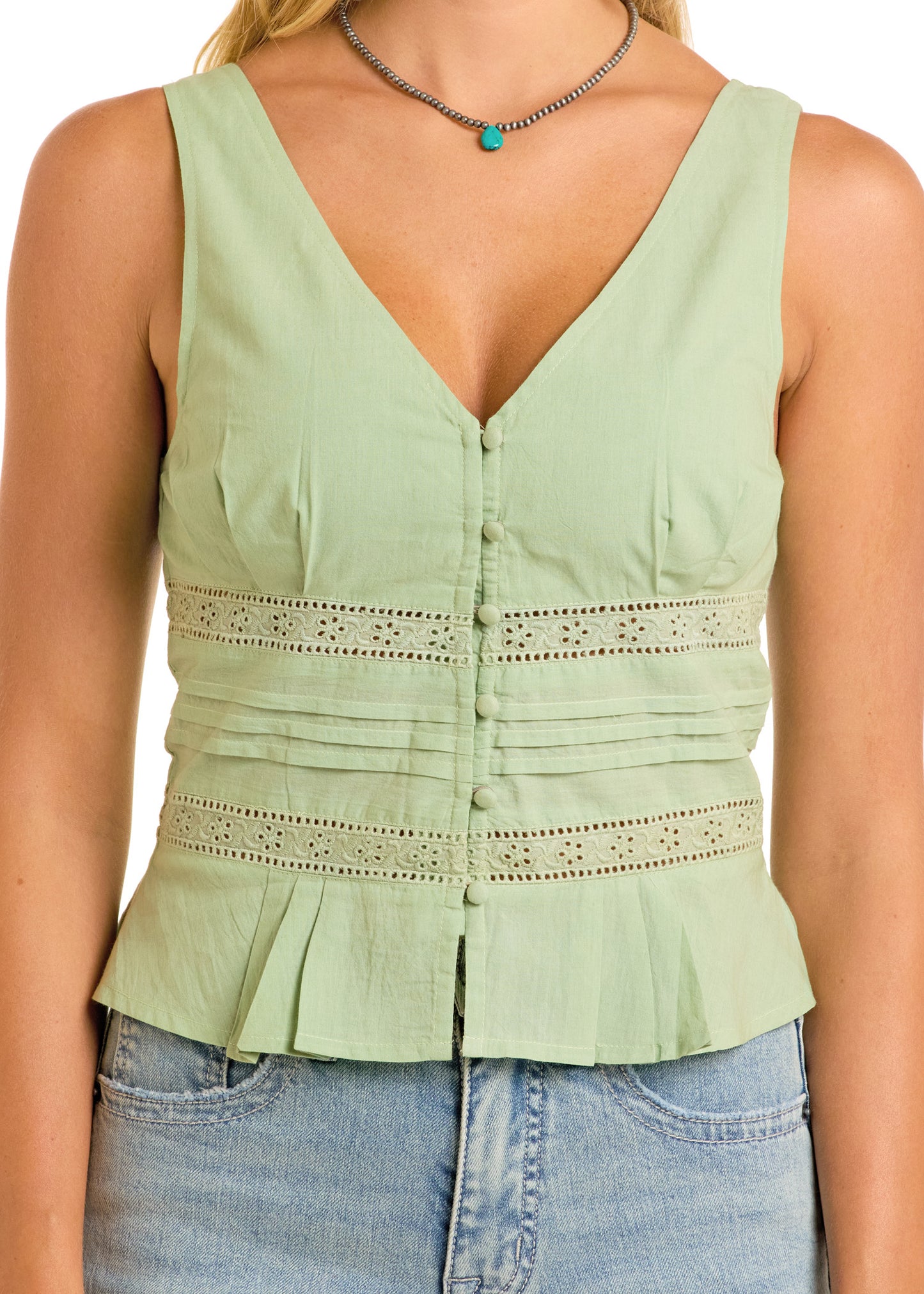 A woman wears the Rock & Roll Denim Eyelet Inset Tank in light green cotton, featuring button details, lace trim, and pleated hem, paired with light blue denim jeans. Only her upper torso is shown.